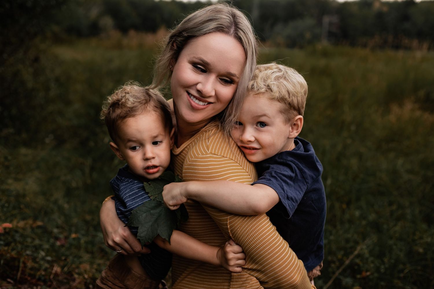 Family hugging and embracing outdoors at golden hour in casual clothing.