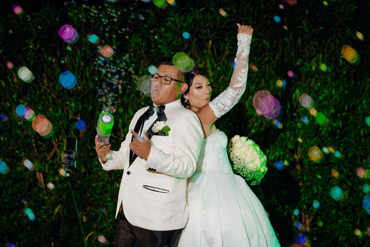 Couple celebrating with confetti and colorful lights against garden backdrop at night wedding.