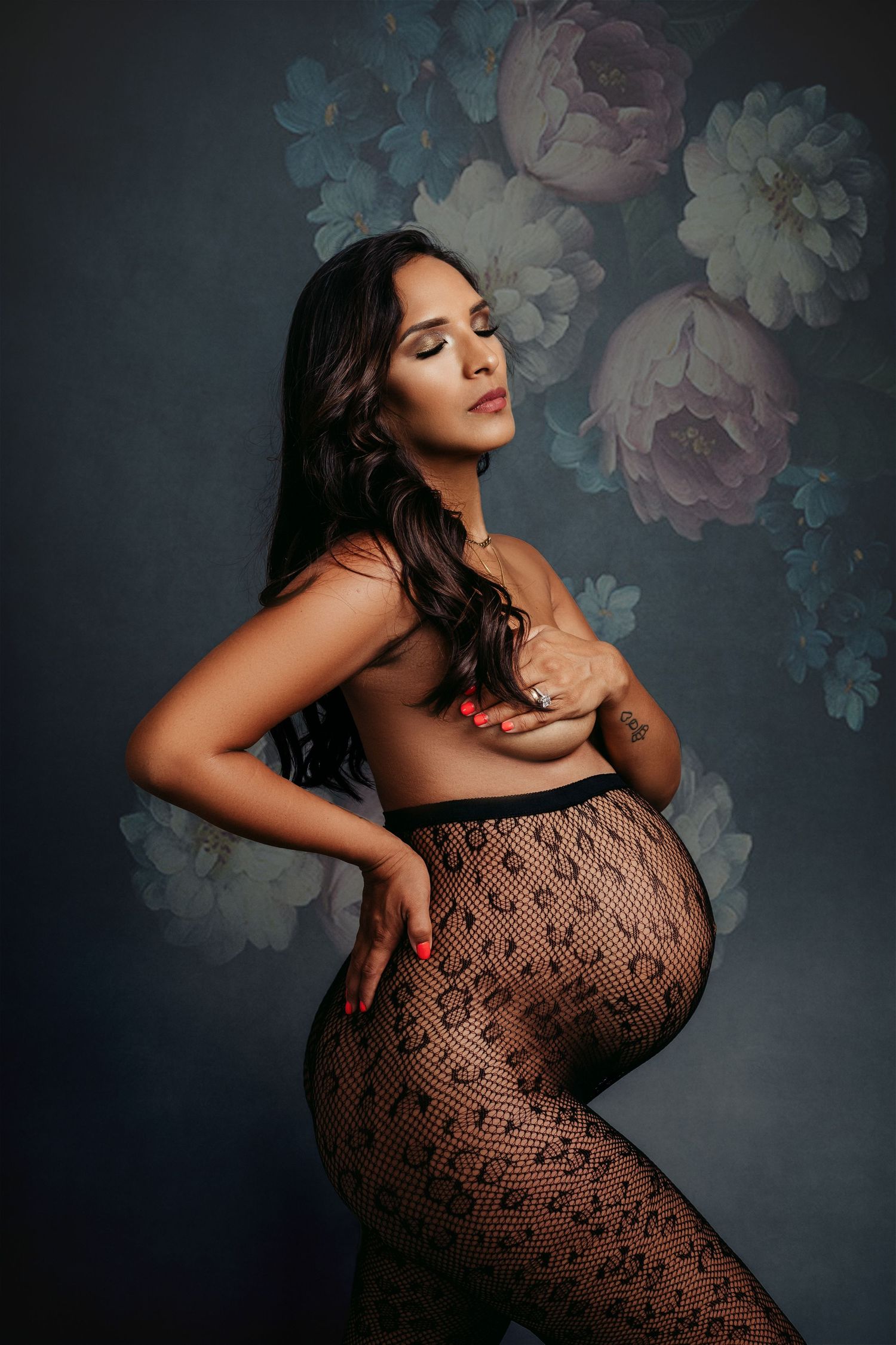 Artistic maternity photo with lace overlay and floral background in moody lighting.