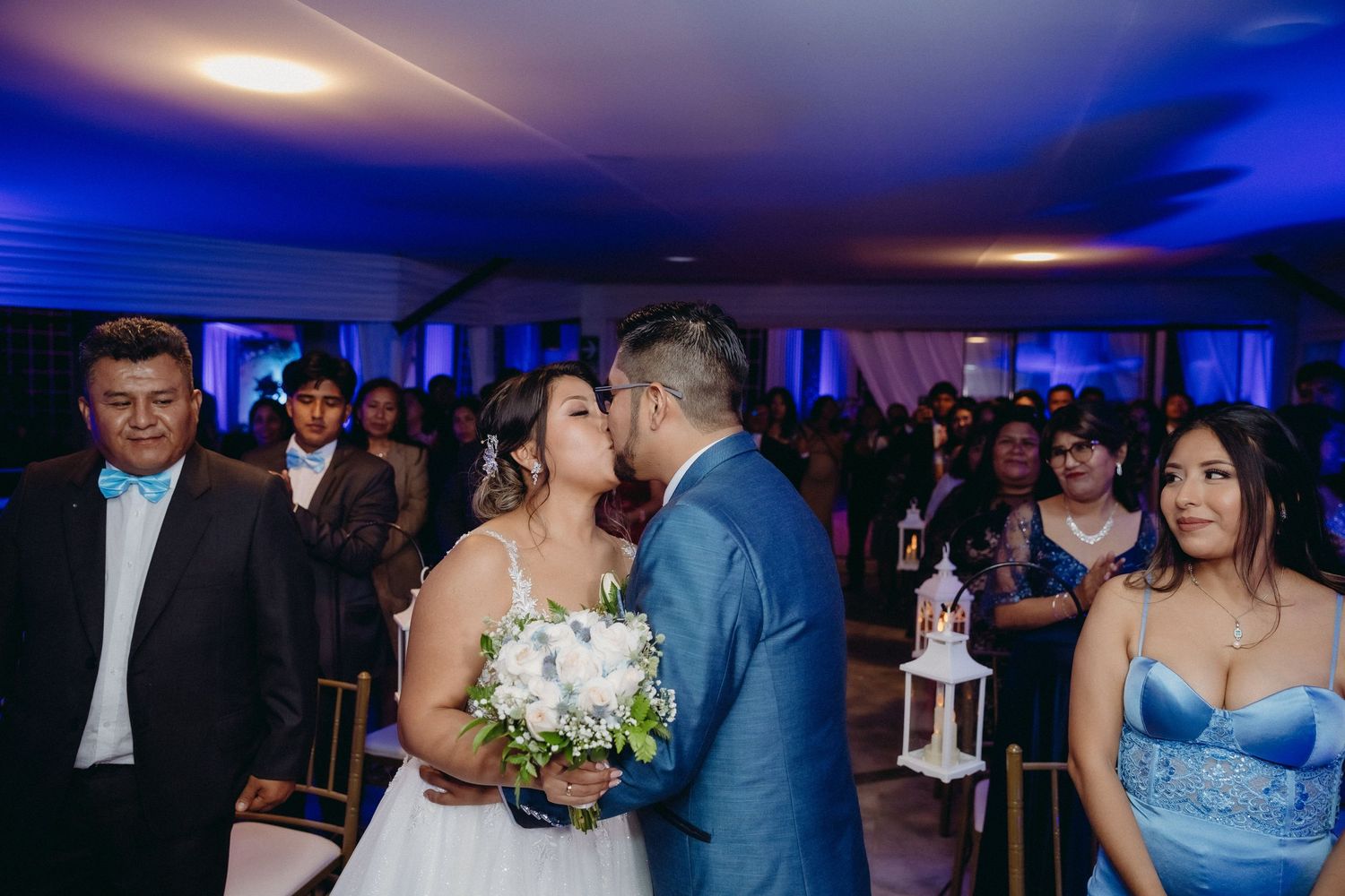 Wedding couple sharing romantic moment during reception with blue lighting and guests in background.