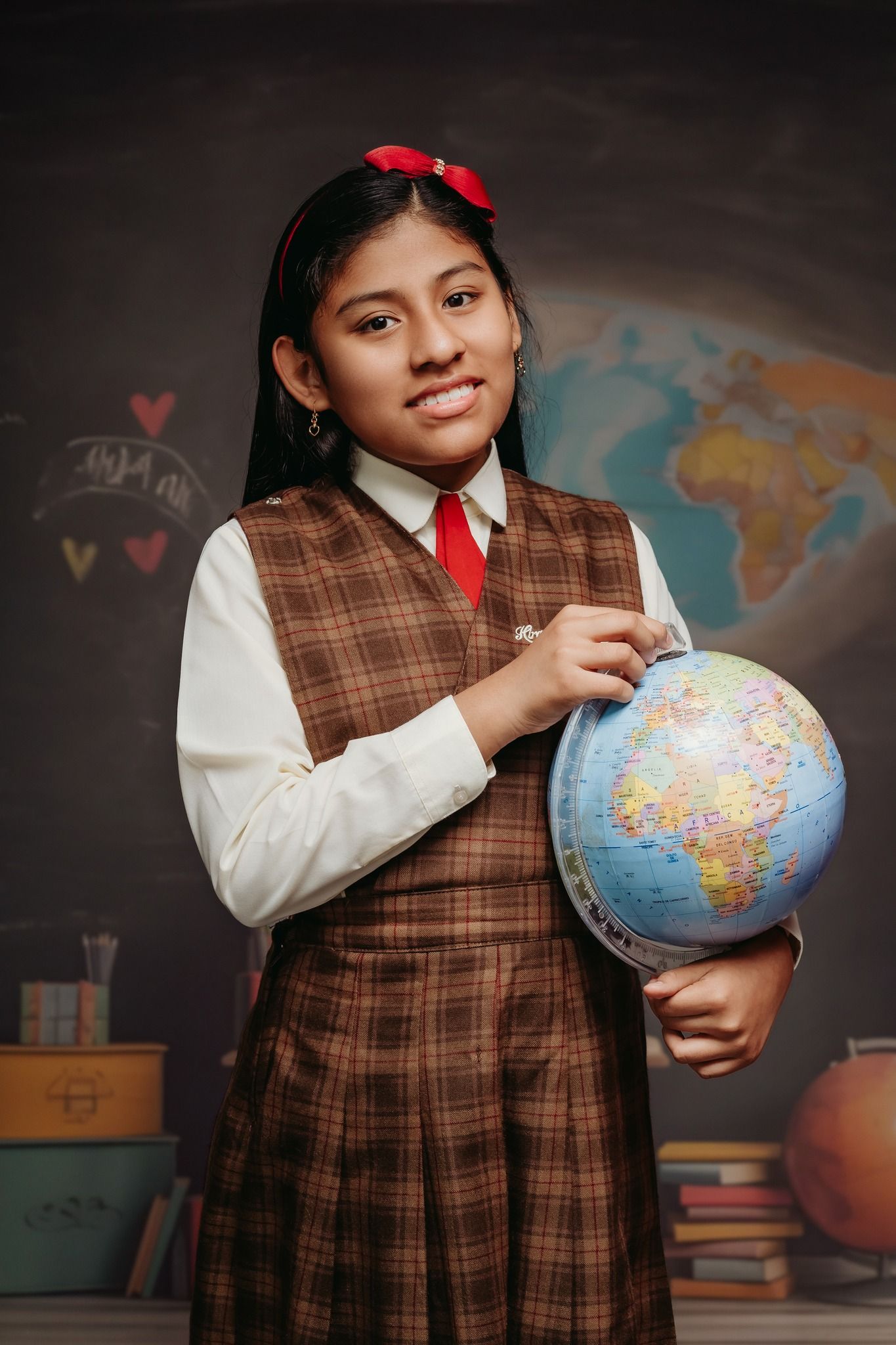 Young student in school uniform poses with globe in front of classroom map.