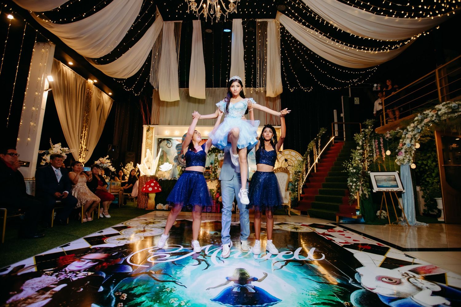 Celebrants dance and pose on an illuminated dance floor under decorative fabric draping and lights.