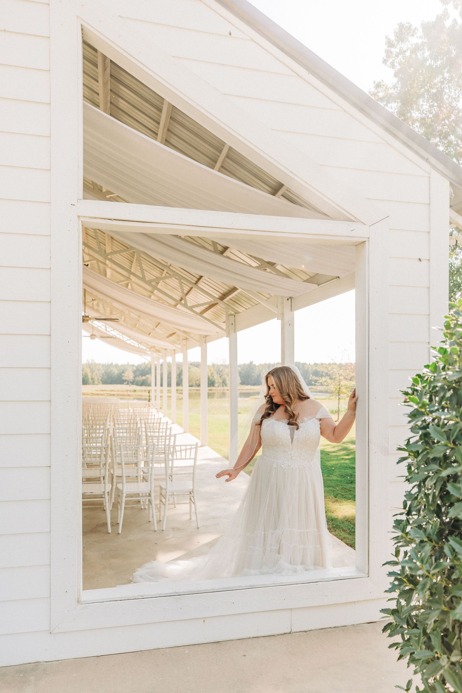 White open-air pavilion with elegant ceremony seating and sunlit backdrop creates a dreamy wedding venue setting.