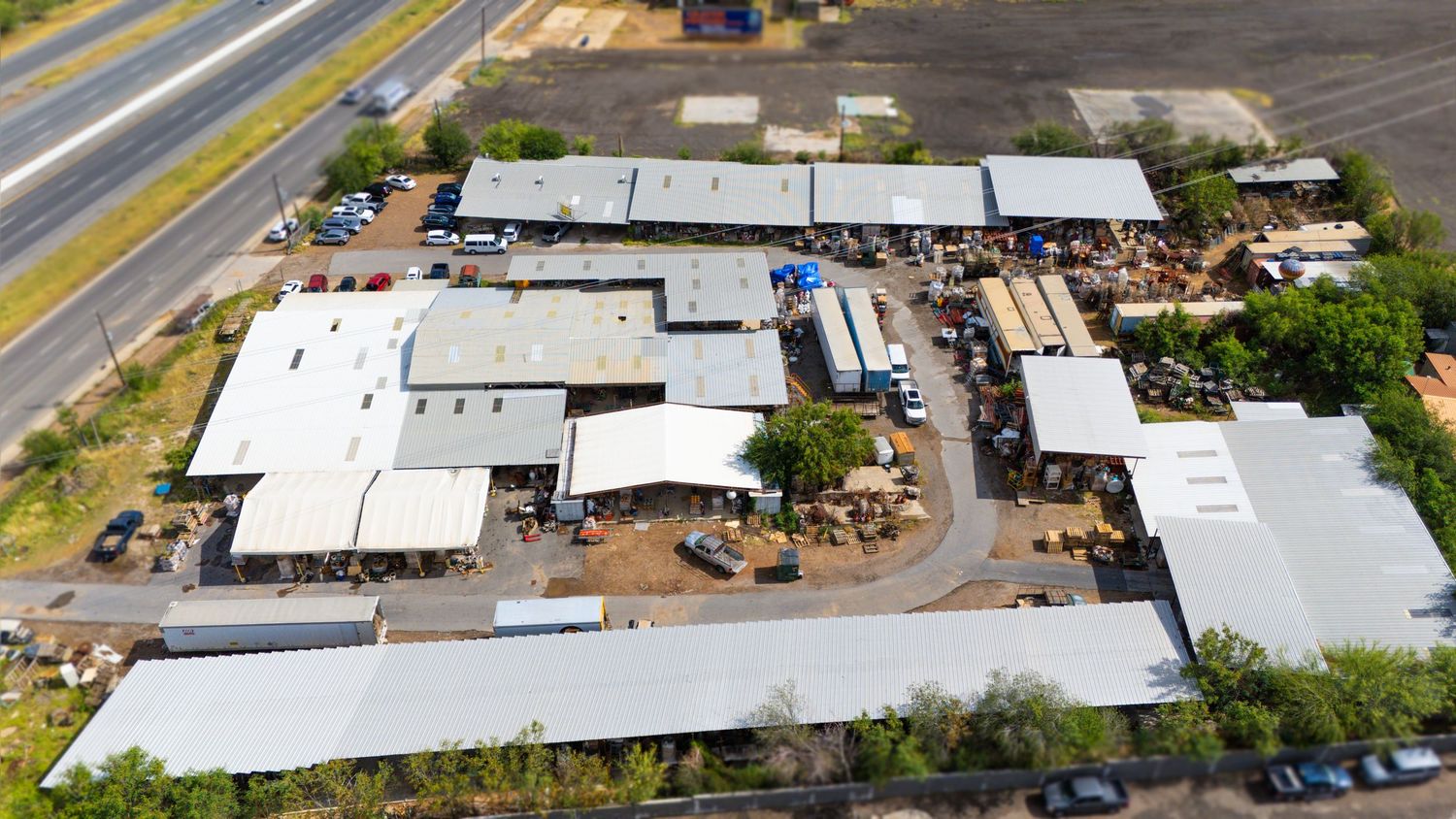 Aerial view of an industrial complex with white-roofed buildings and storage yards surrounded by paved areas.