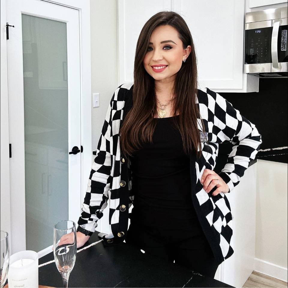 A black and white checkered cardigan paired with a black top in a modern white kitchen setting.