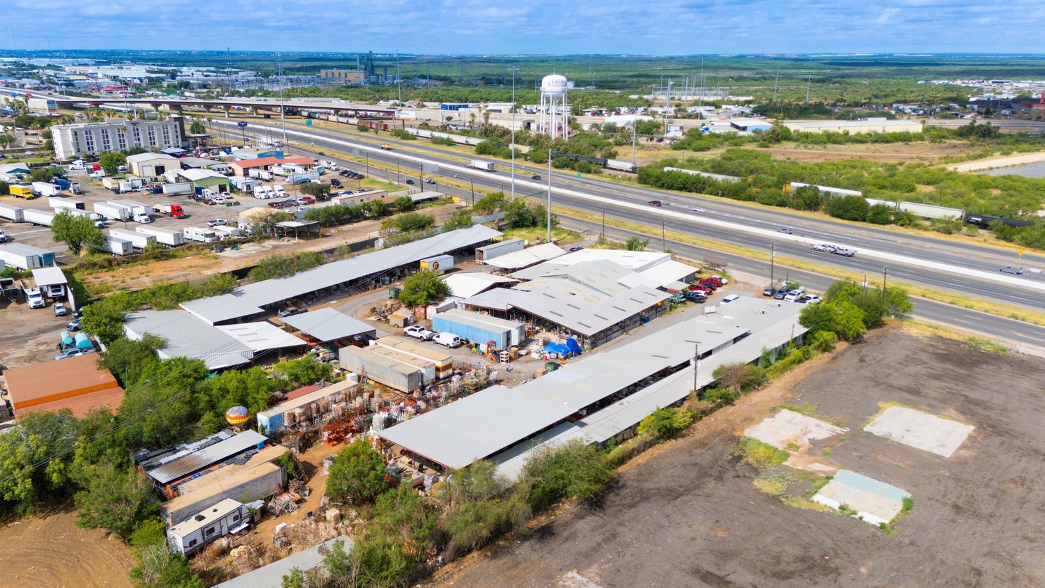 Aerial panoramic view of industrial buildings and warehouses with white roofs surrounded by development plots.