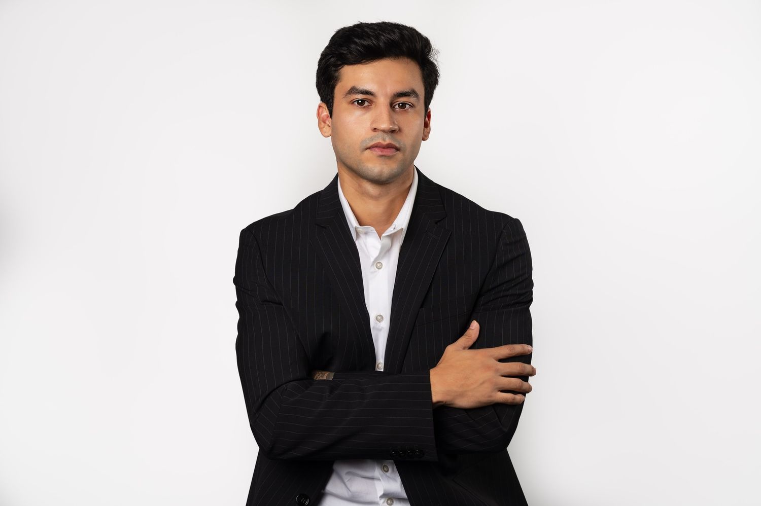 Professional portrait of a person wearing a black blazer and white shirt standing with arms crossed against white background.