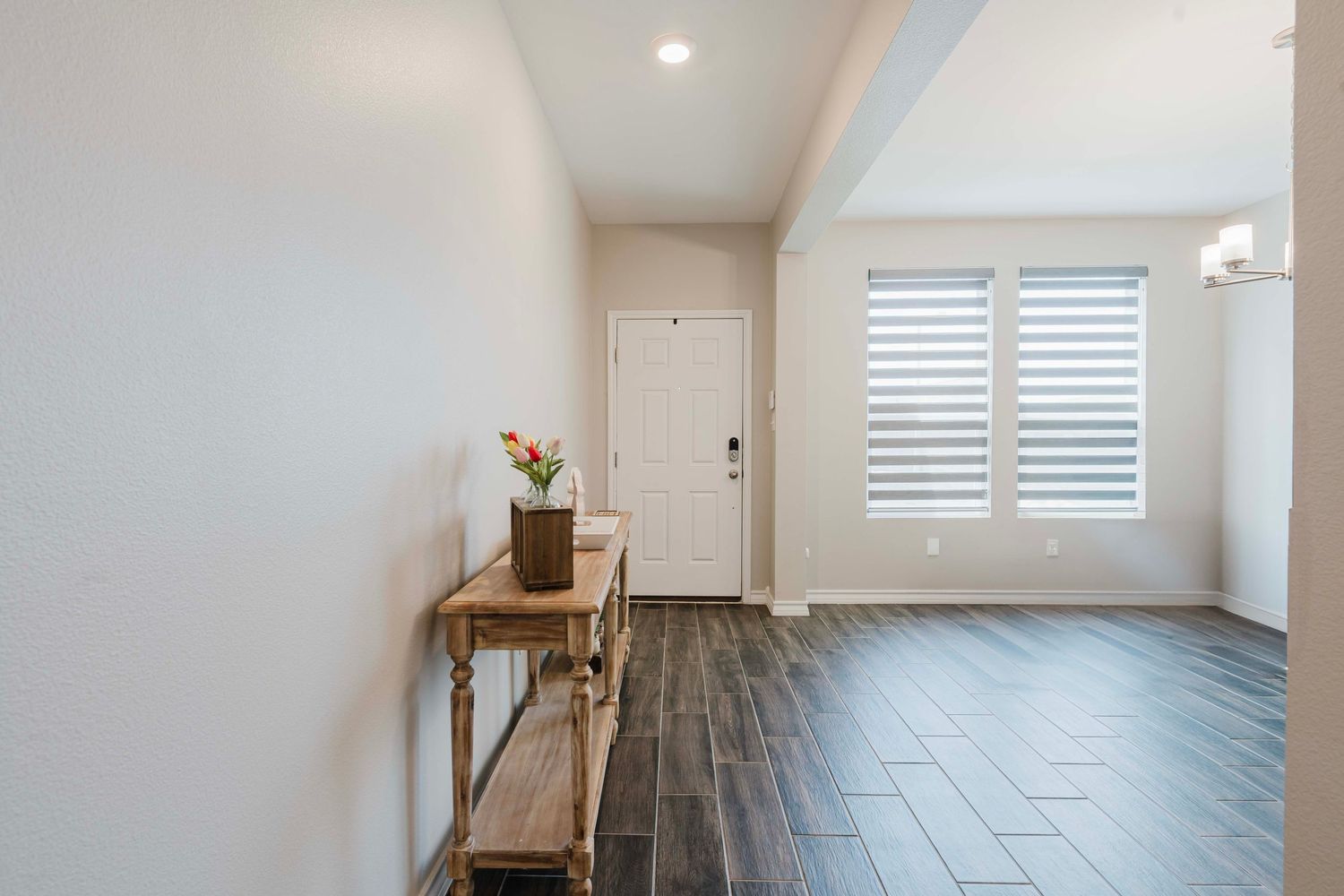 Modern entryway with wood console table, dark hardwood floors and white walls featuring plantation shutters.