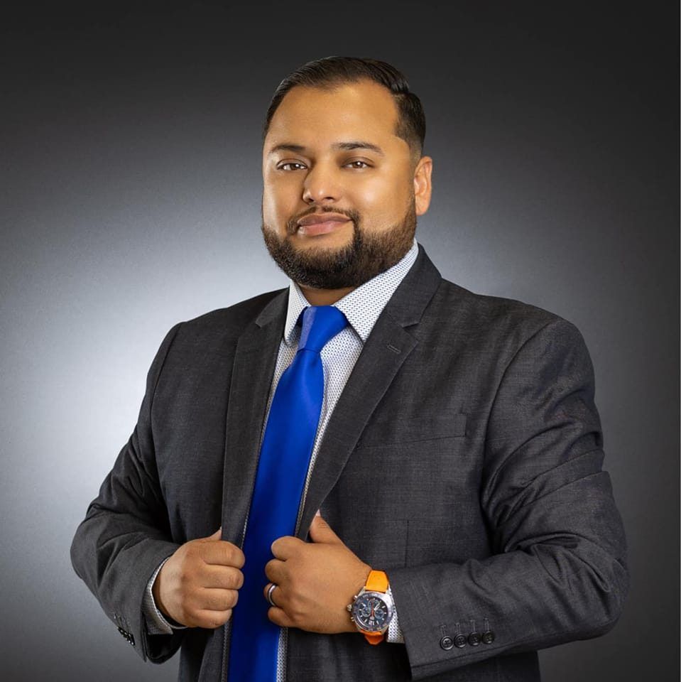 Professional headshot of a businessman in a dark suit and bright blue tie against a gradient gray background.