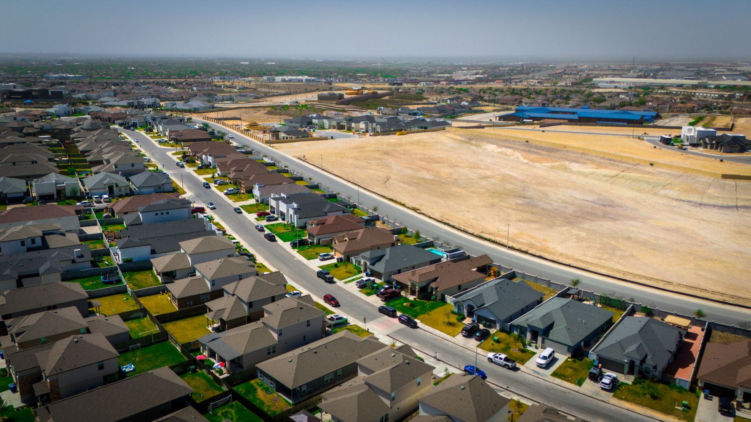 Aerial view of a new residential development with rows of houses and empty lots under construction beside a cleared area.