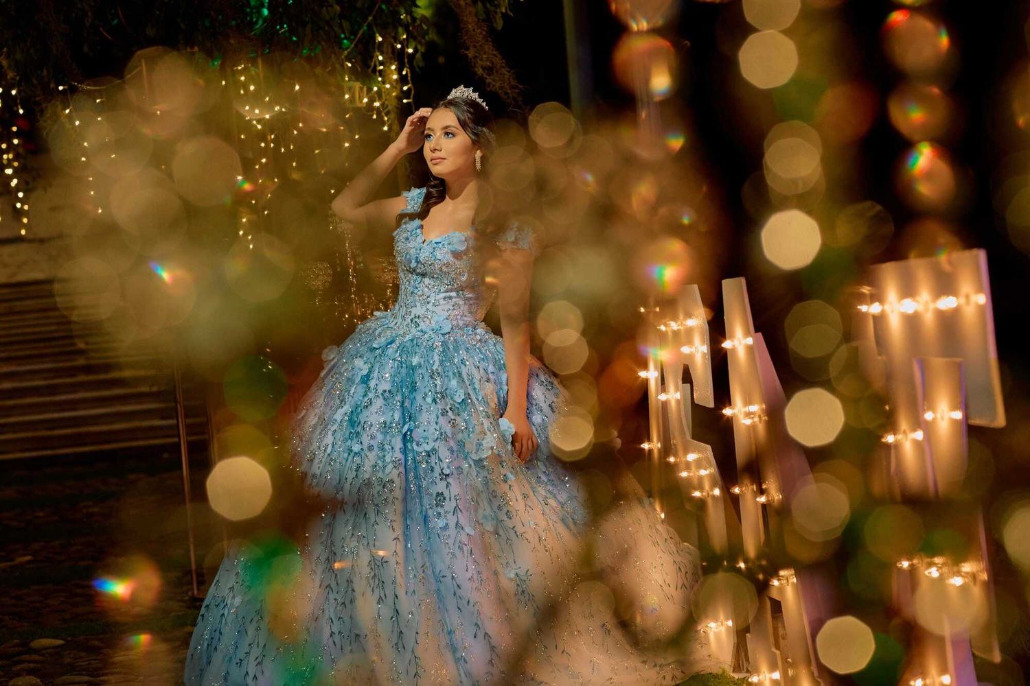 A figure in a blue ballgown stands amidst glowing bokeh lights and candles creating a dreamy, ethereal atmosphere.