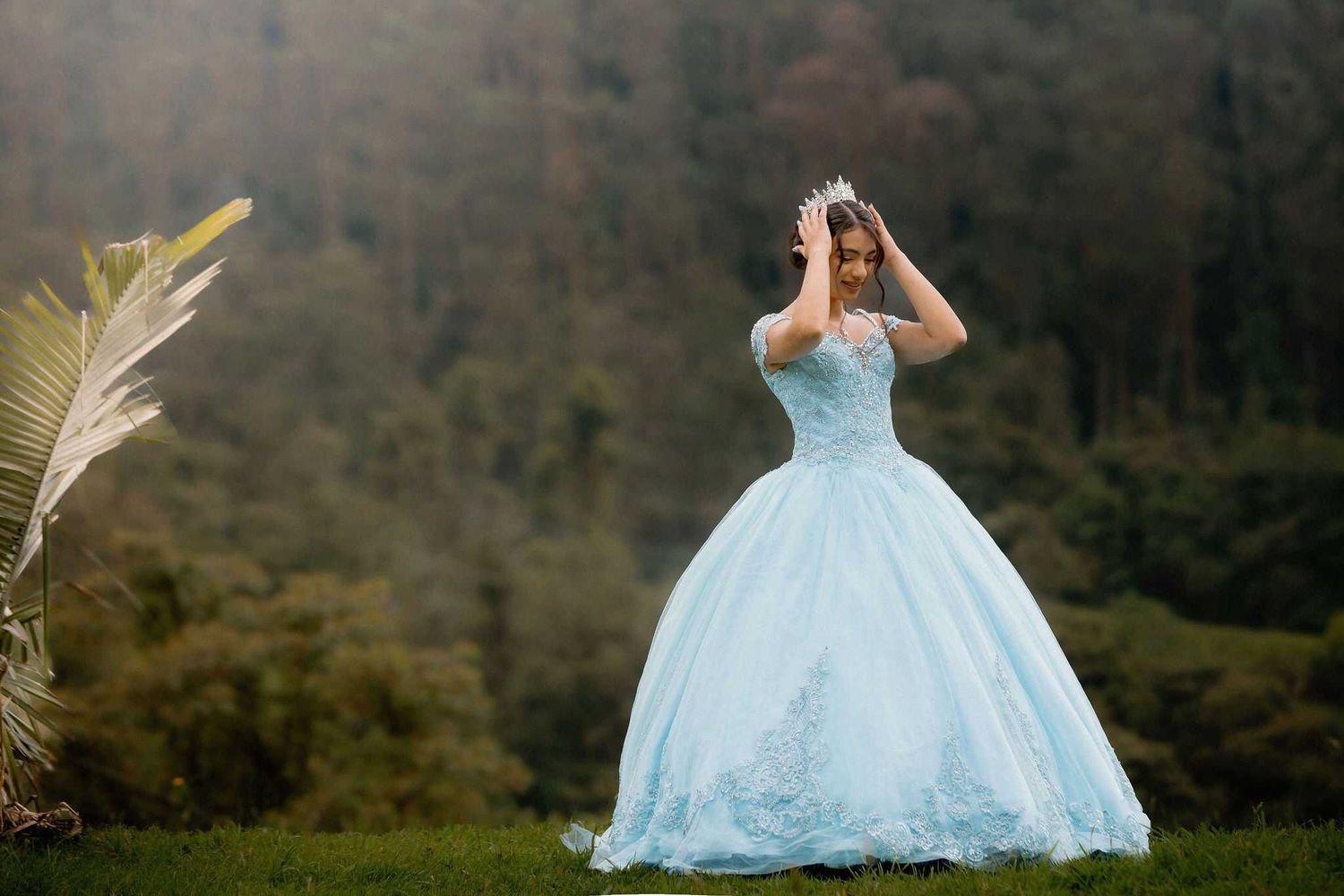 A bride in a flowing white ball gown poses in a misty forest setting surrounded by tall trees.