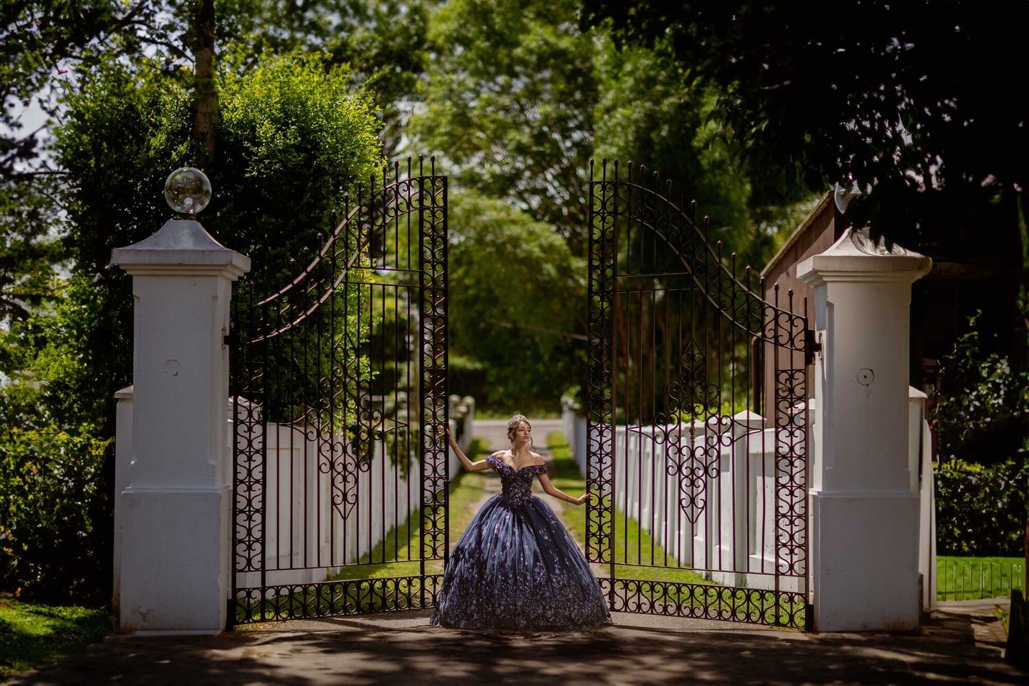White ornate garden gate and stone pillars lead to a lush green estate garden path.