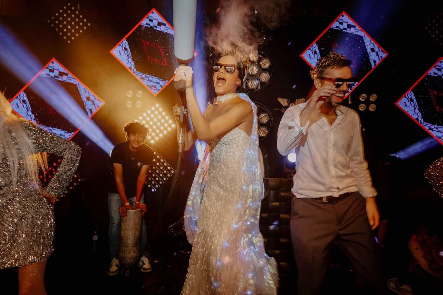 Vibrant dance party scene with people dancing under geometric light decorations at a wedding reception.