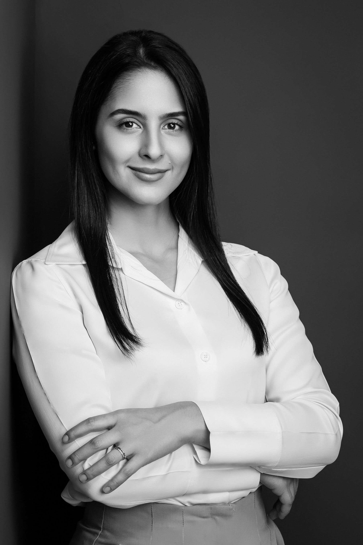 Professional studio portrait of a smiling person in a white business attire with long dark hair, against a dark background.