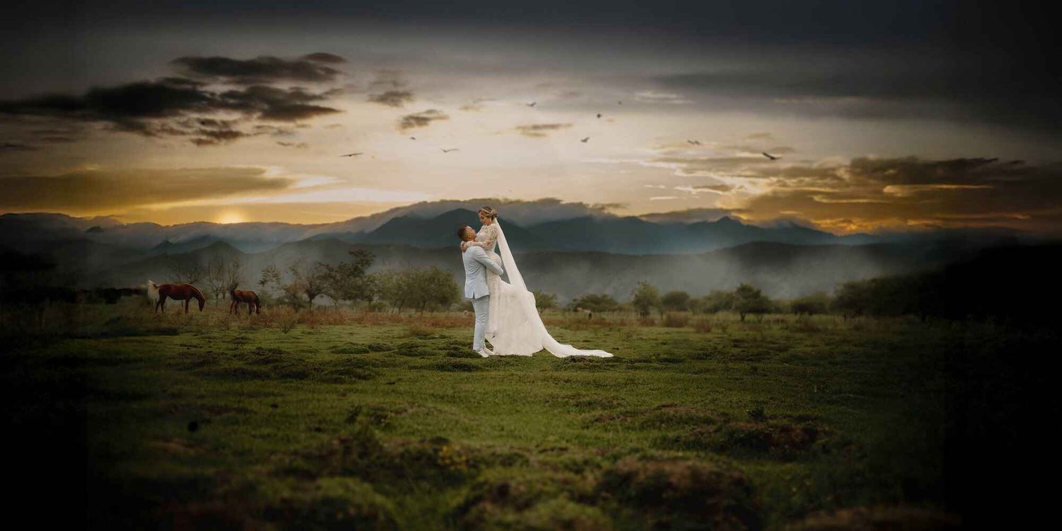 A figure in a white gown stands in a vast open field at sunset with mountains and dramatic clouds in the background.