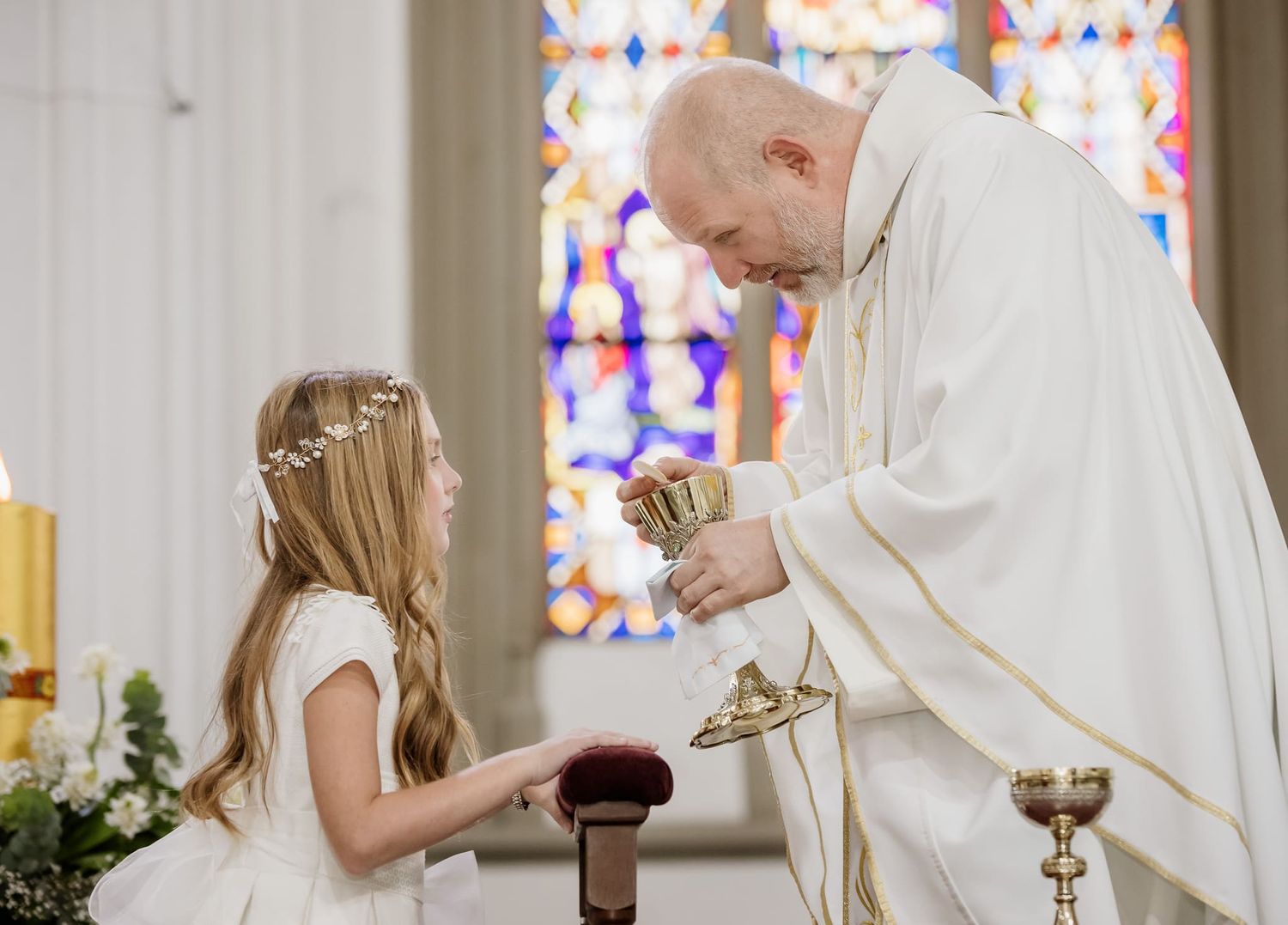 foto de primera comunion durante la ceremonia nina recibiendo comunion del sacerdote en iglesia 2024