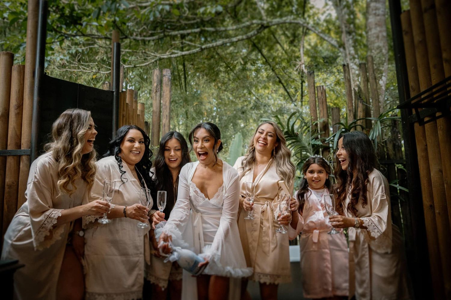 Novia y amigas riendo juntas durante los preparativos con copas de vino.