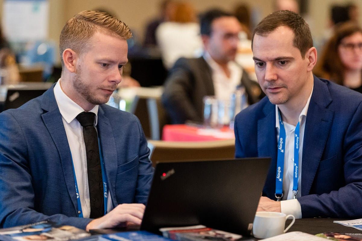 Two business professionals in suits review information together on a laptop during a conference meeting.