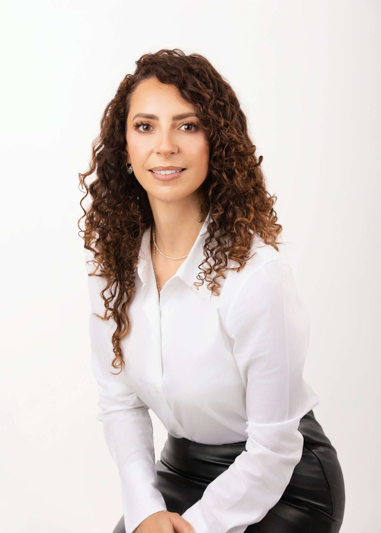 Professional portrait of someone with long curly dark hair wearing a white button-up shirt against a light background.