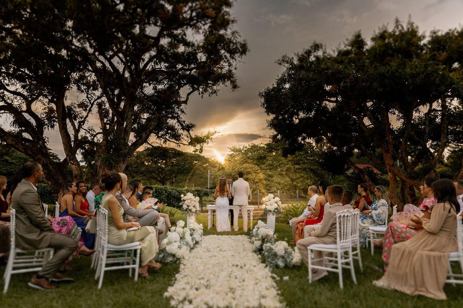 Ceremonia de boda sencilla entre árboles y flores con invitados reunidos.