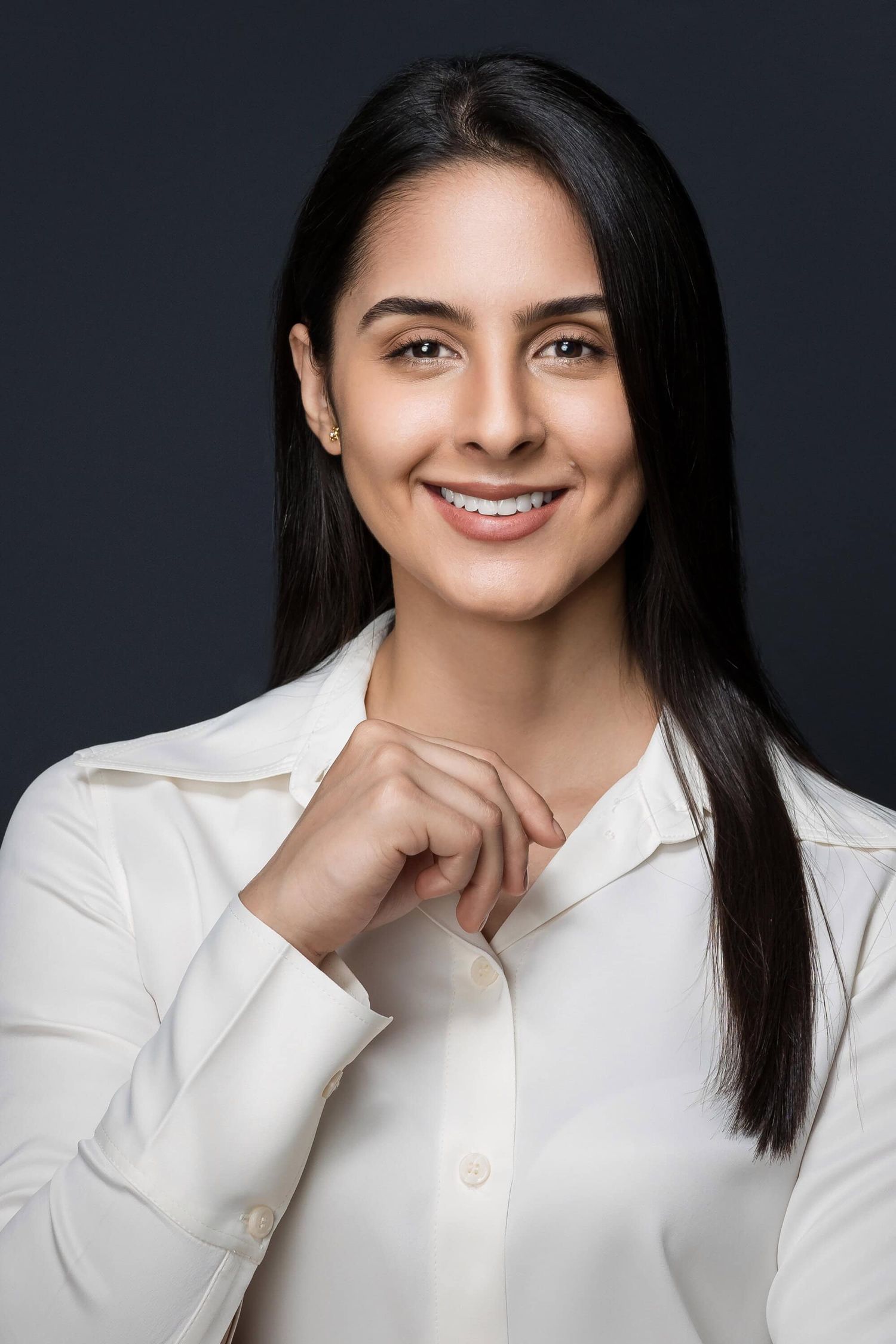 Professional portrait of a person with long dark hair wearing a white button-up blouse against a dark background.