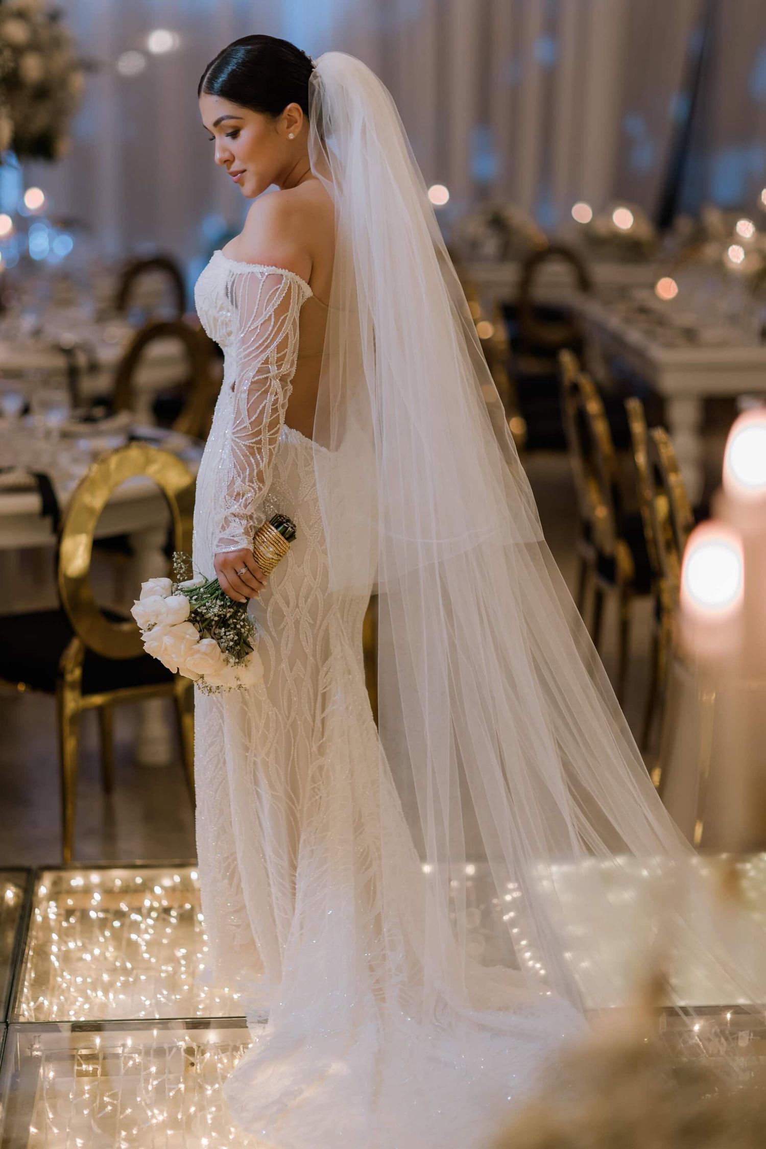 Novia de espaldas con vestido blanco y velo largo en recepción elegante