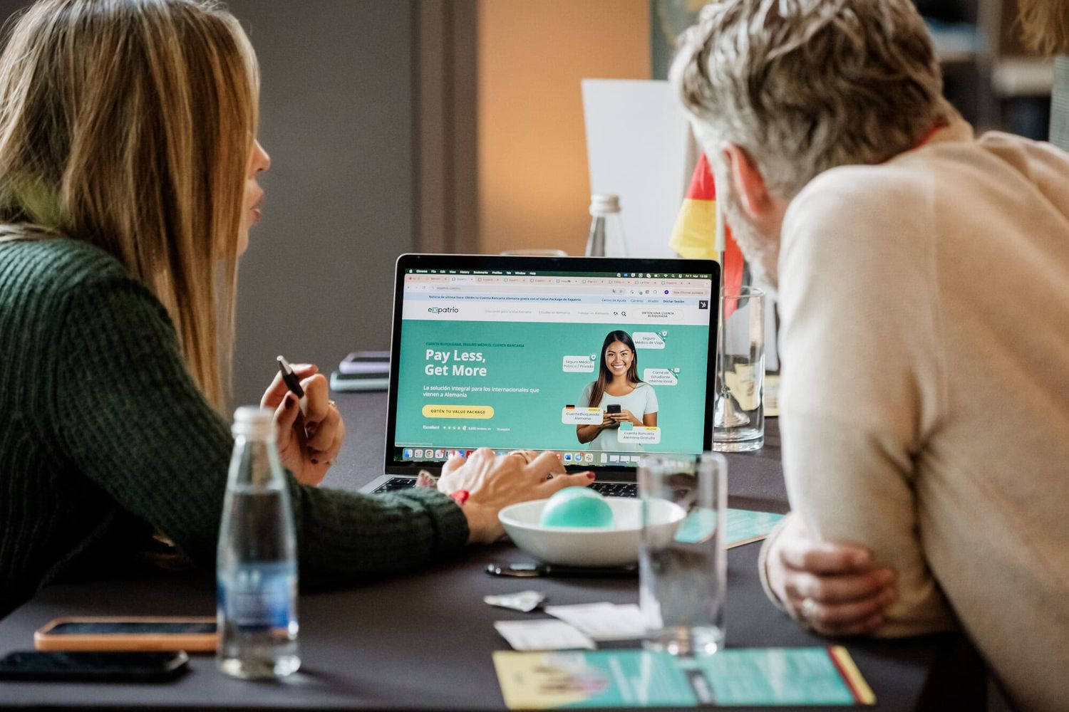 Two professionals looking at computer screen showing video conference interface during business meeting.