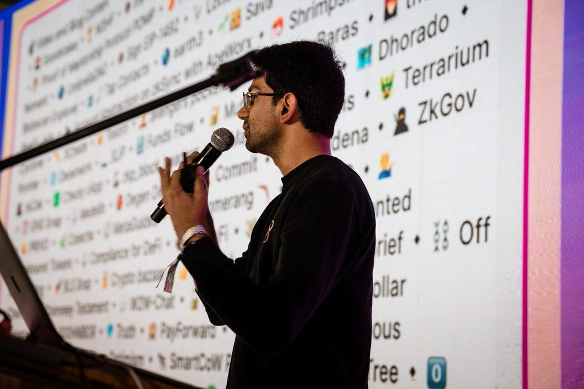 Speaker presenting in front of large projection screen displaying computer interface during tech presentation.