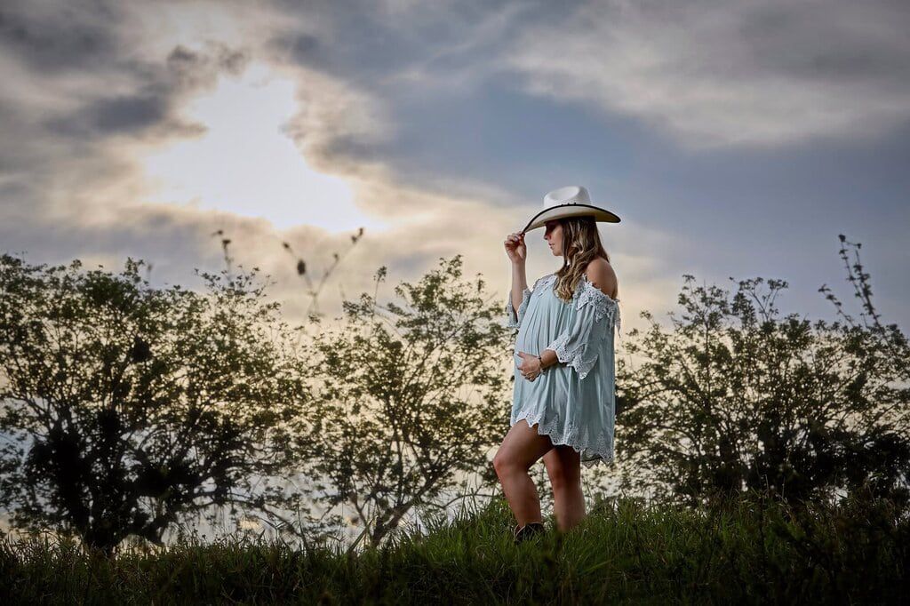 A silhouette stands in a sundress and hat against a dramatic sunset sky with wildflowers blowing in the breeze.