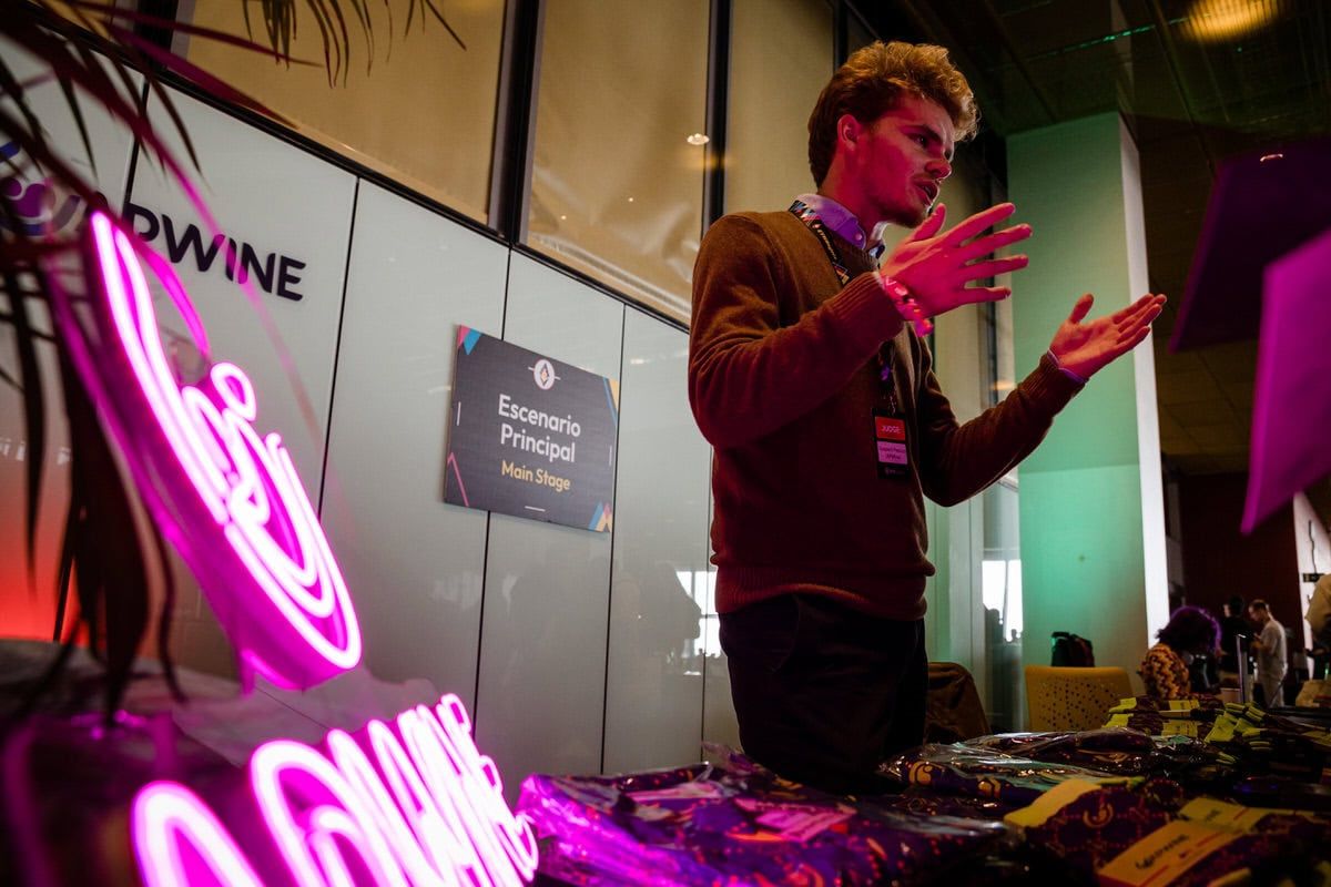 DJ performing at event with pink neon wine sign in background while working equipment.