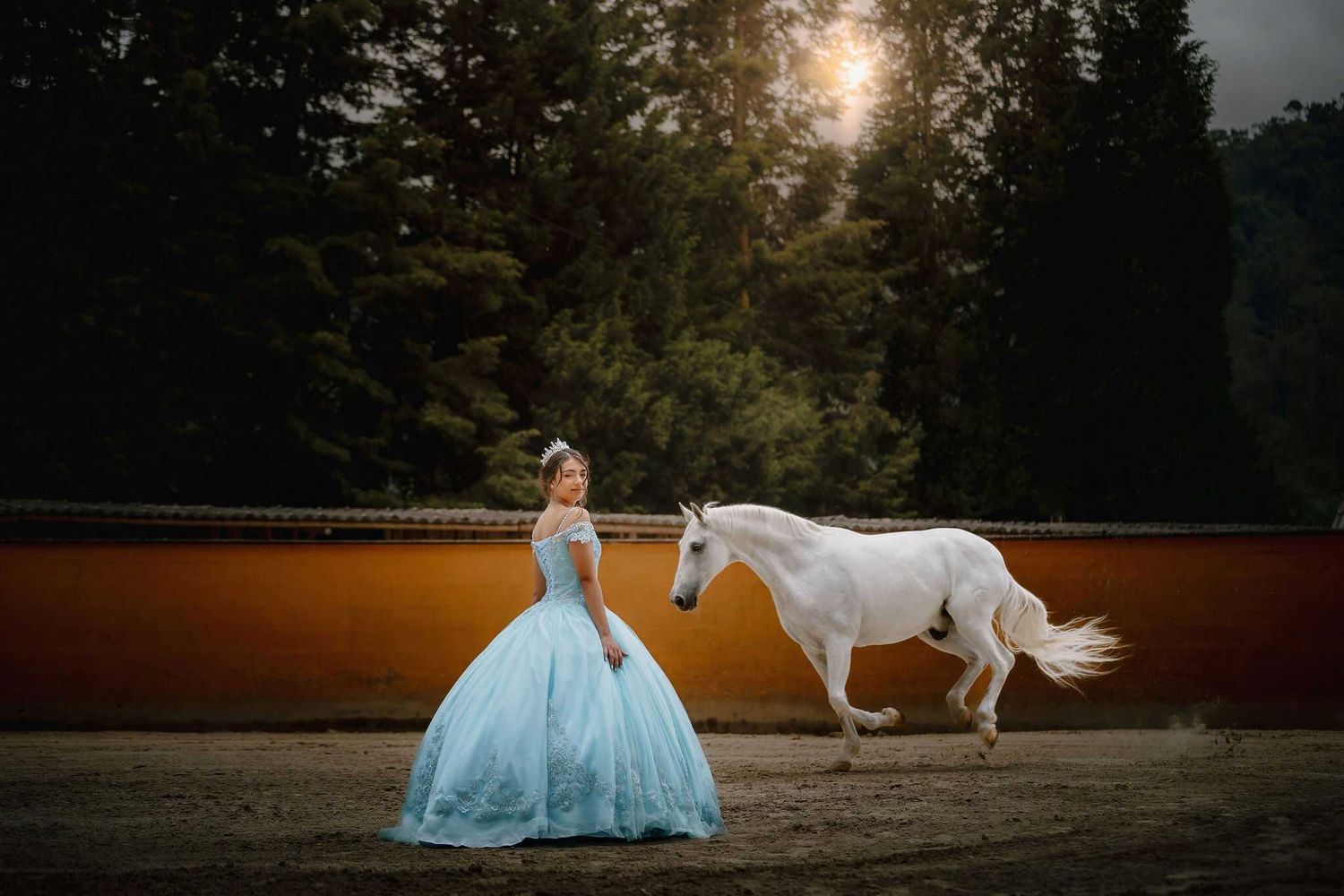Ethereal scene of a person in a flowing blue ballgown standing beside a majestic white horse at sunset.