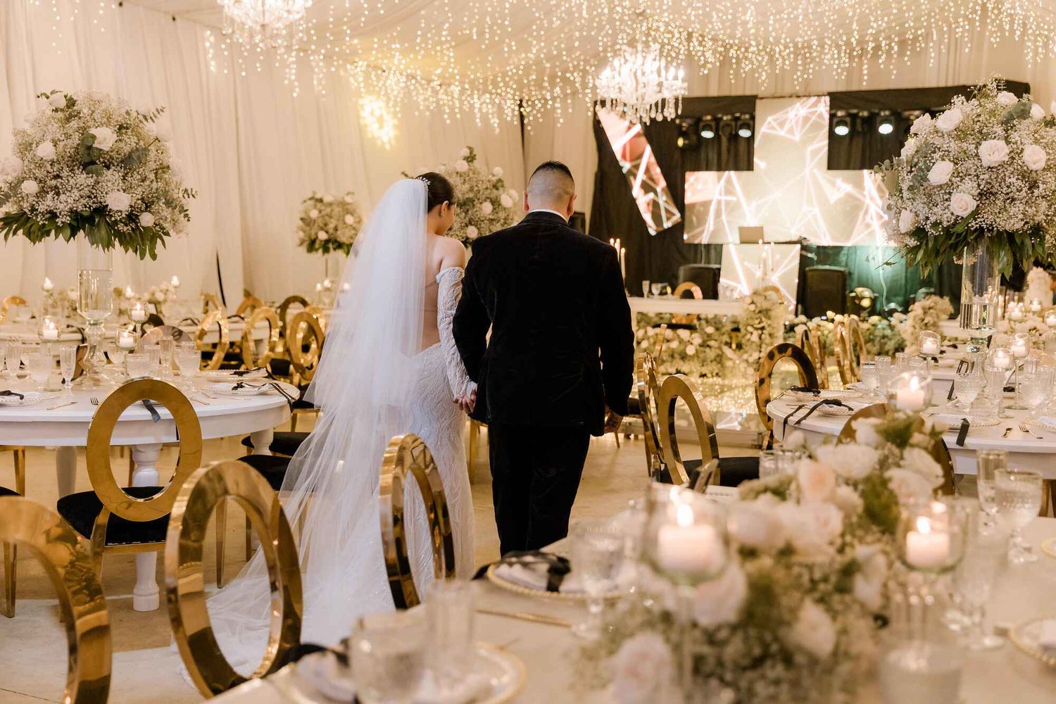 Pareja de novios entrando a la recepción, rodeados de decoración elegante y mesas floridas
