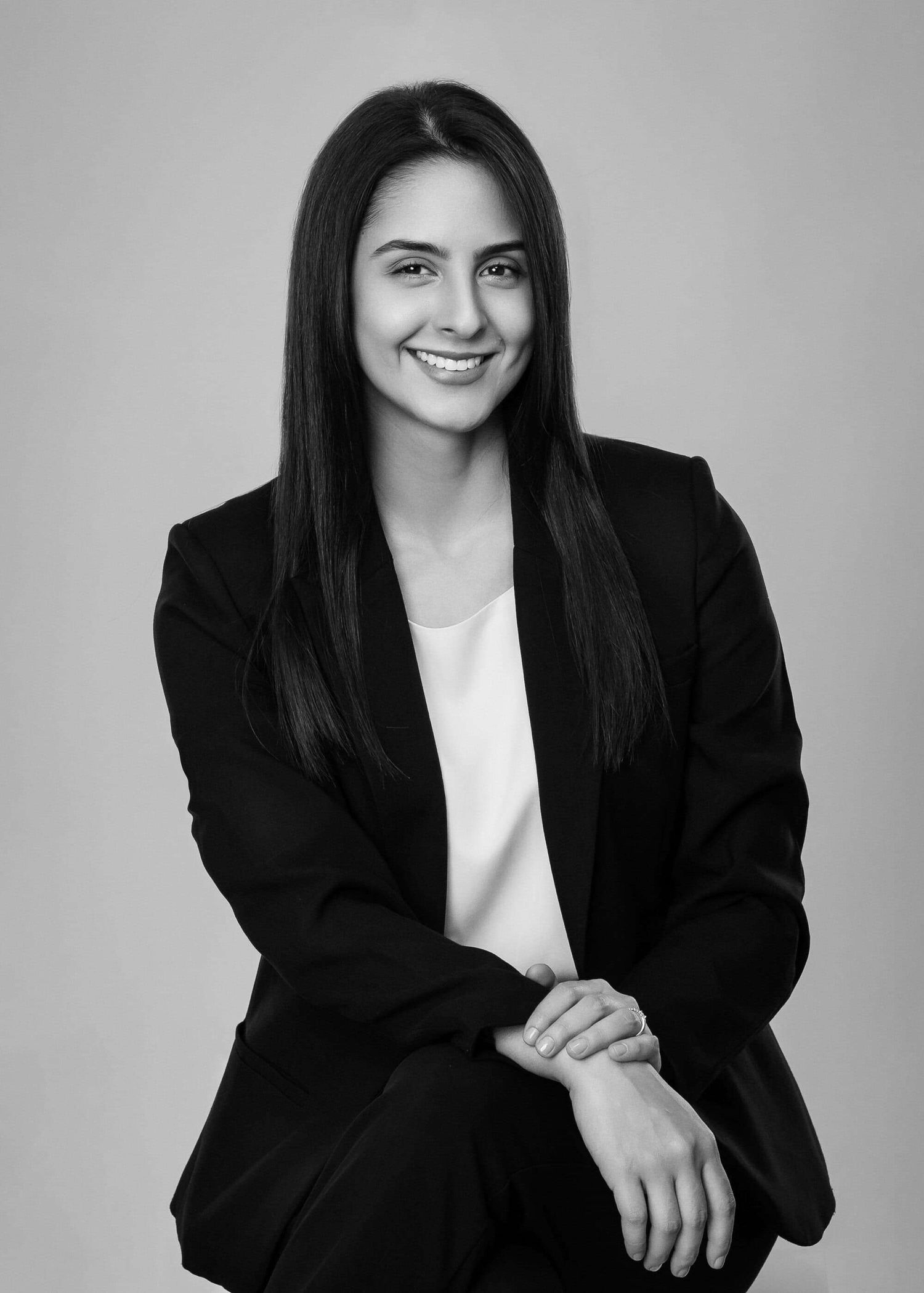 Professional black and white portrait of person in dark blazer and white top smiling against neutral background.