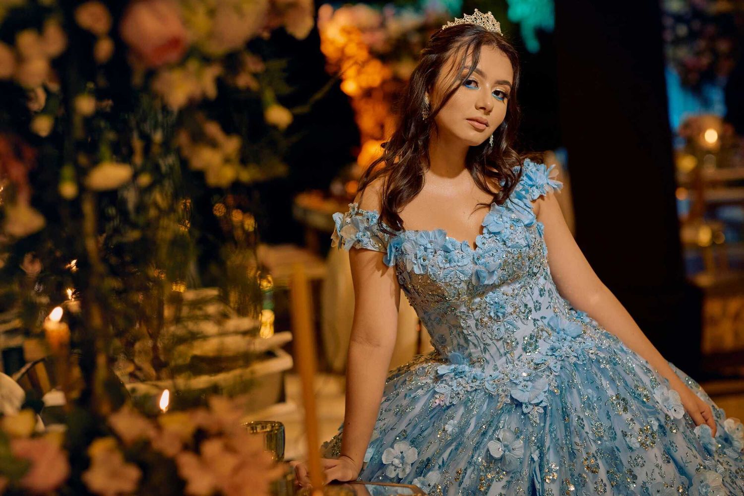 An elegant model in a light blue princess gown poses among glowing autumn foliage at night.