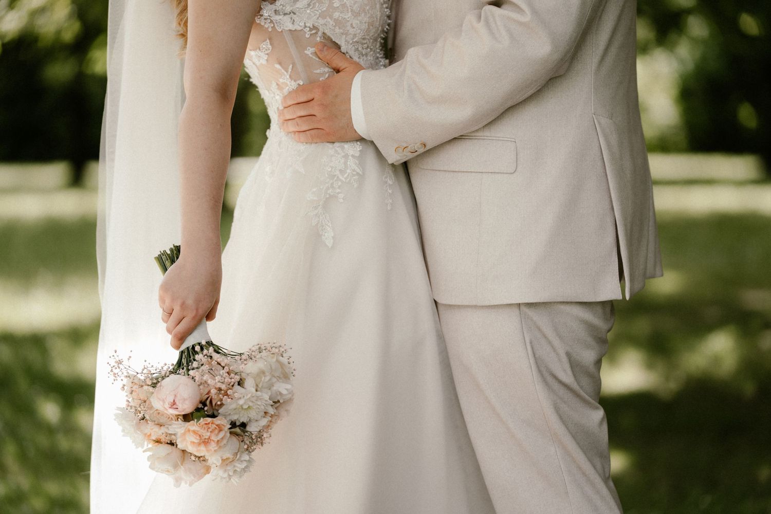 A romantic wedding couple shares tender moments in a garden setting while holding a delicate pink and white bouquet.