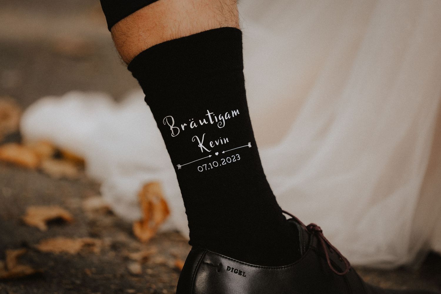 Black socks with white text are photographed against a rustic wooden surface with scattered autumn leaves.