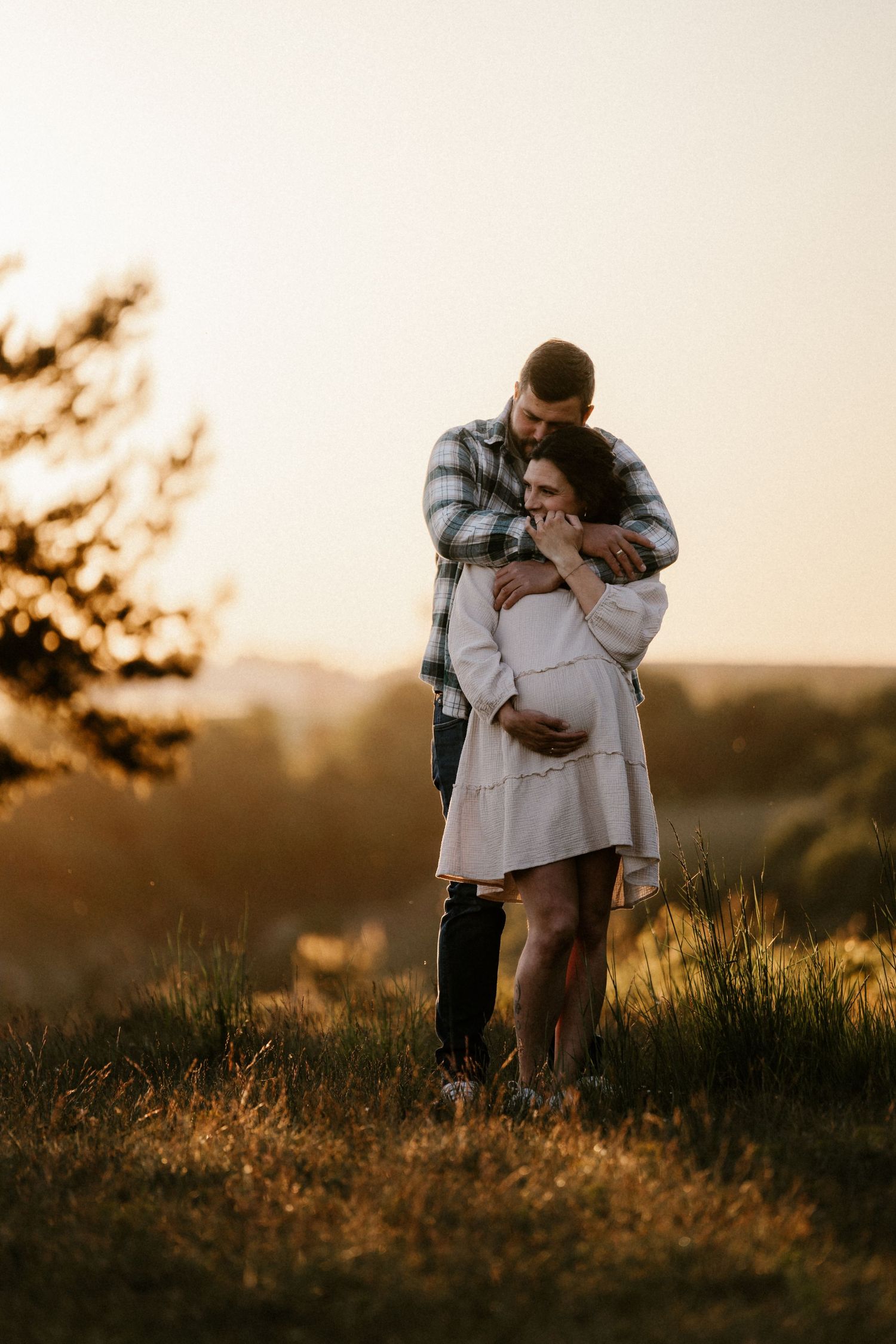A couple embraces in a romantic moment during golden hour sunset in a grassy field.