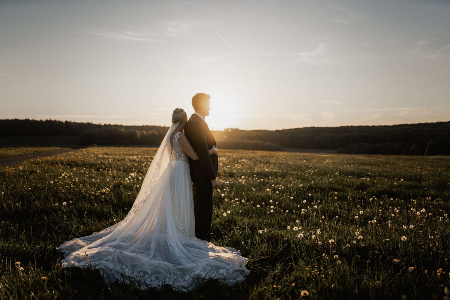 A couple shares a romantic moment in a sunlit meadow filled with wildflowers during sunset.