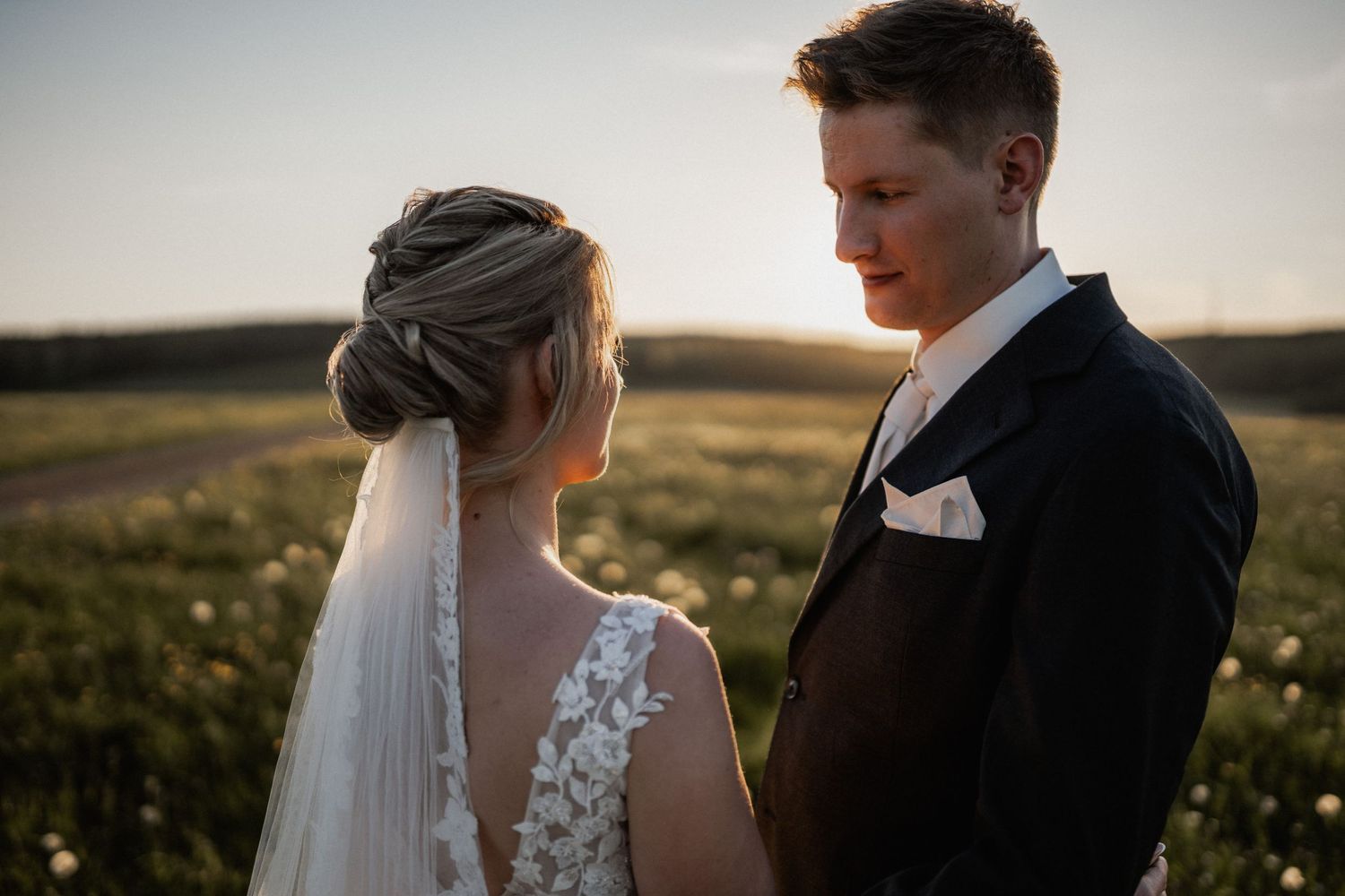 A bride and groom stand close together in a golden field at sunset.