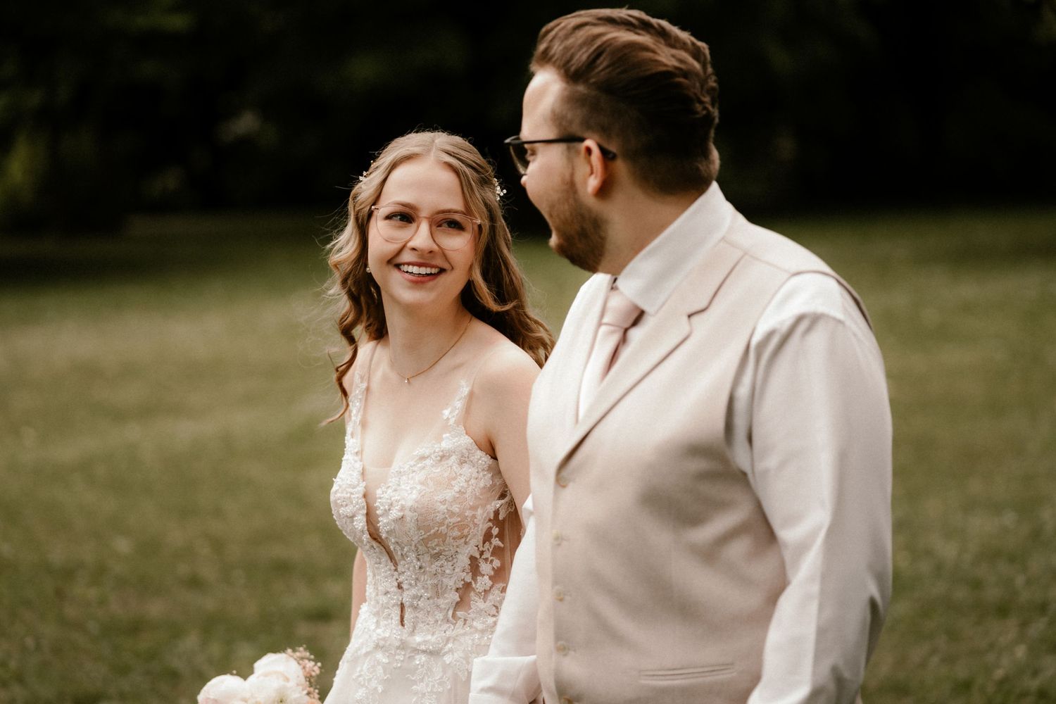 A happy bride and groom share a joyful moment together outdoors in neutral-toned wedding attire.