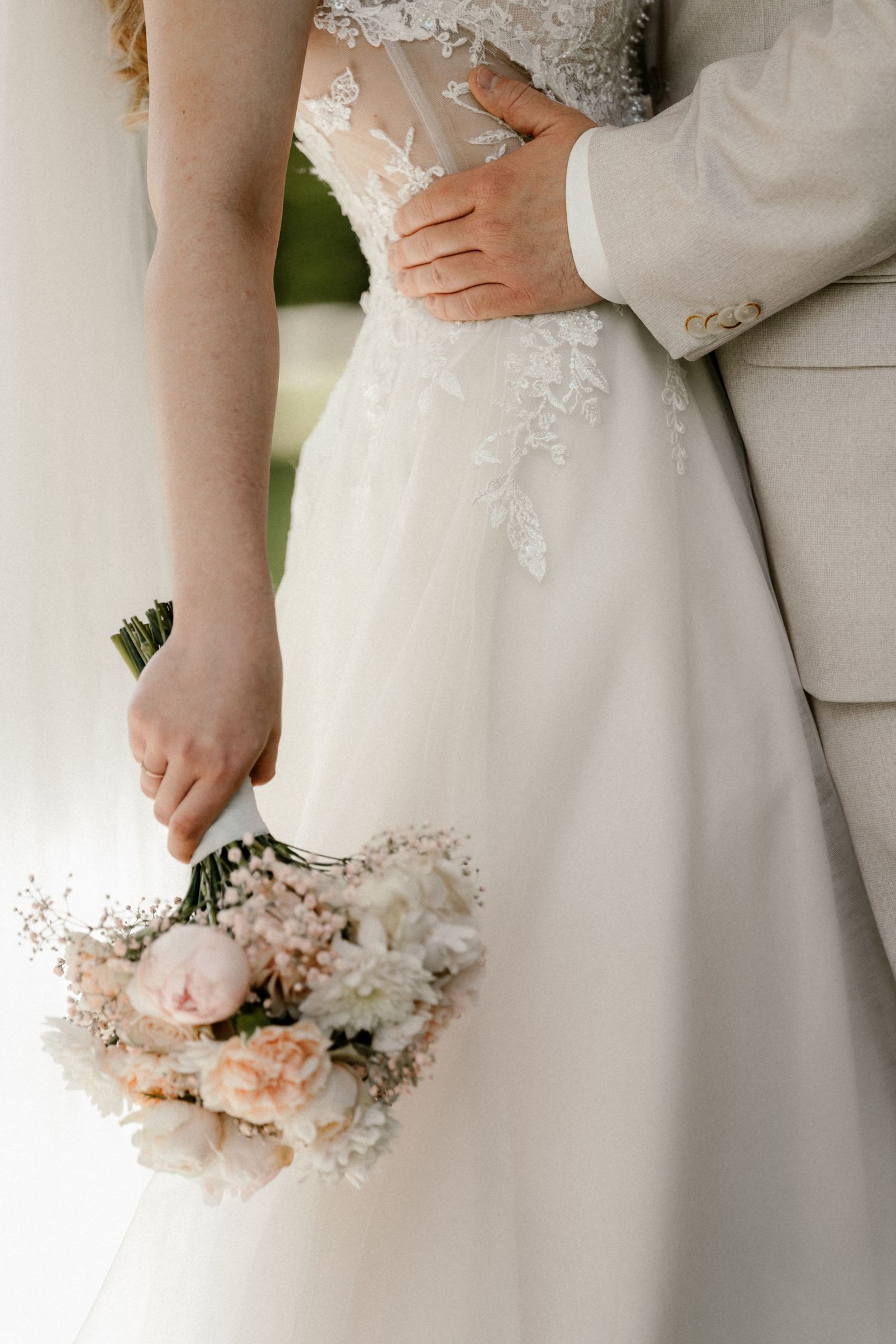 A delicate wedding bouquet of pink roses and baby's breath held against a white lace bridal gown.