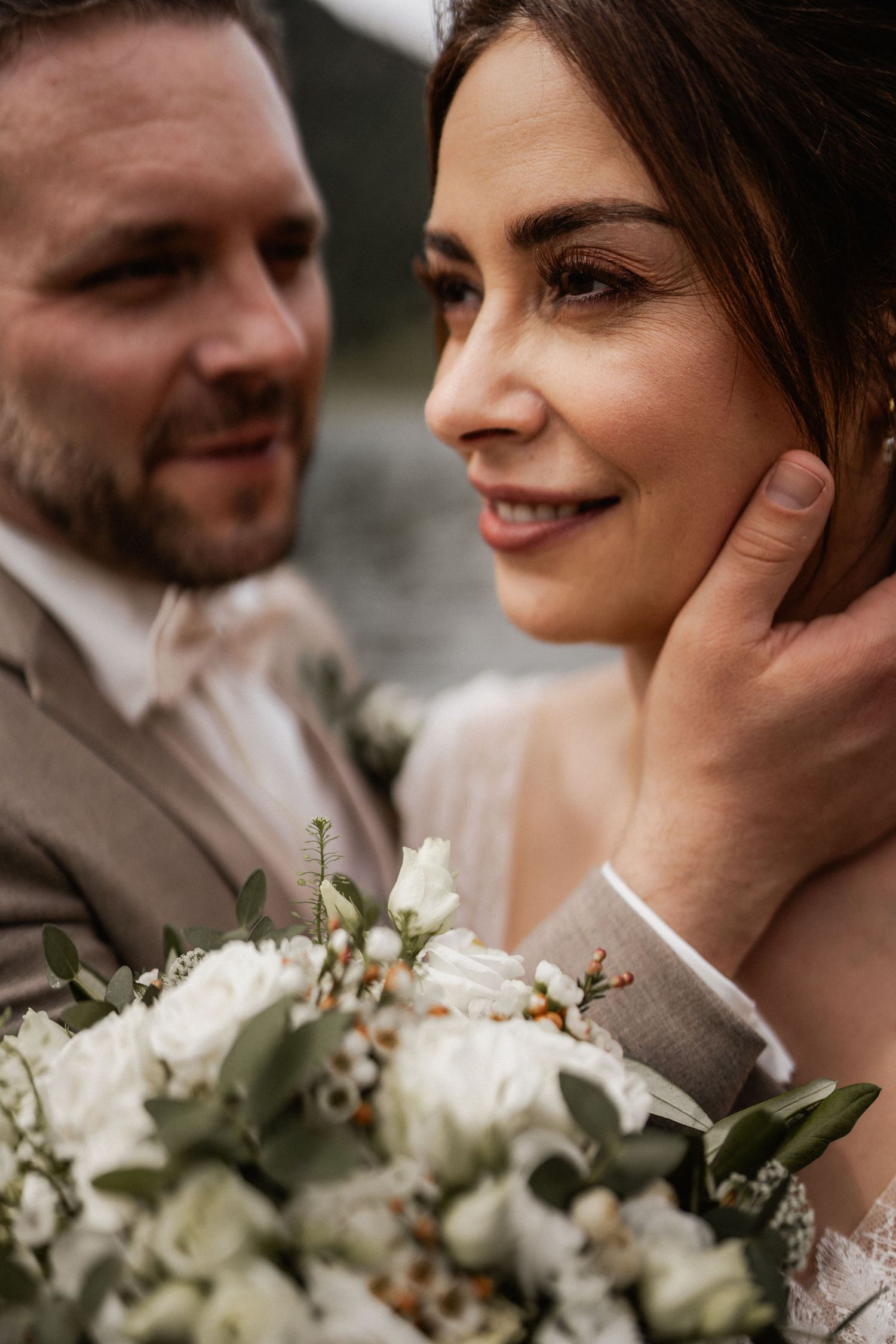 Intimate wedding moment with elegant white bouquet featuring roses and greenery in a moody lighting style.