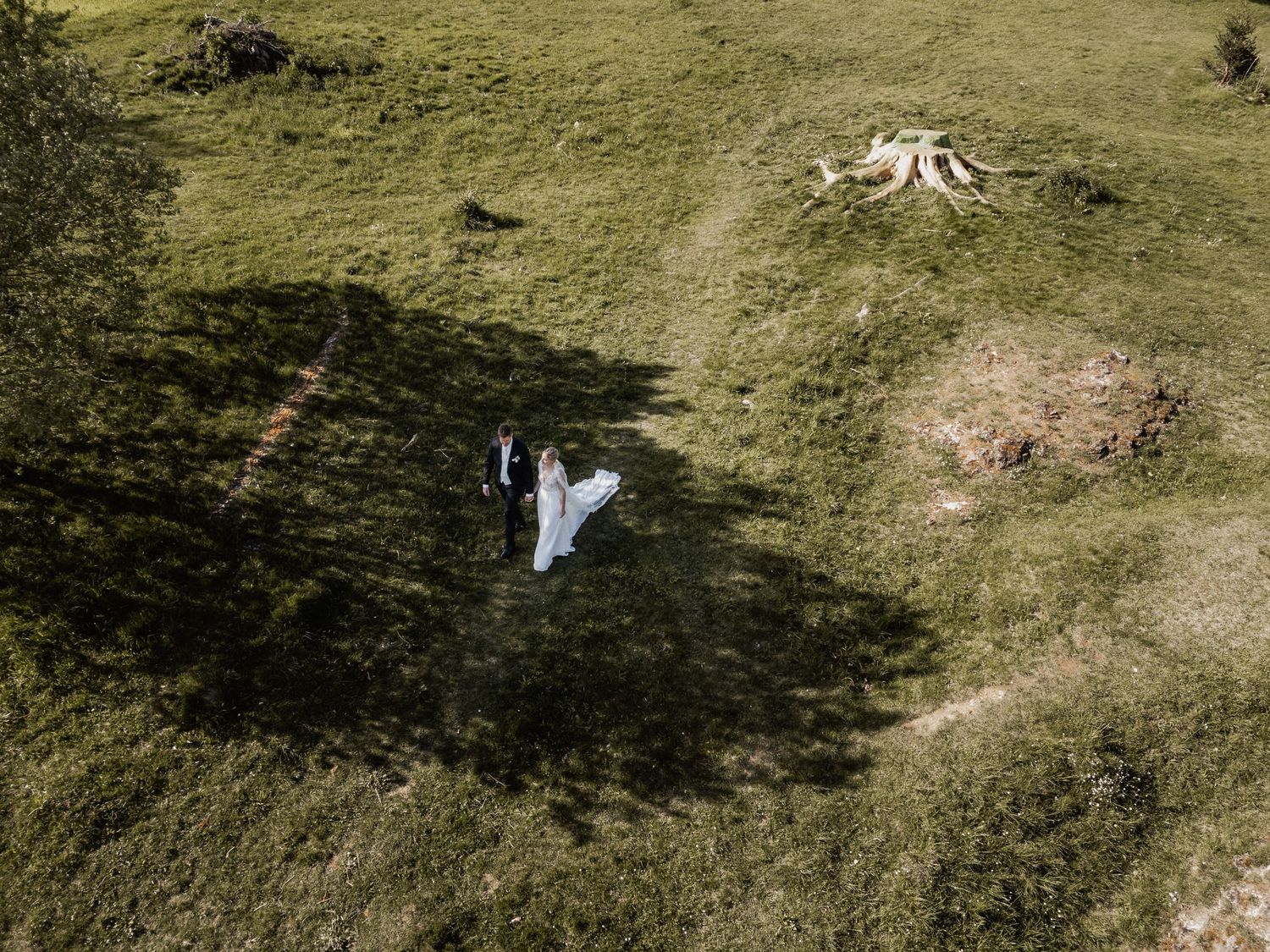 Aerial view of a white wedding dress on green grass field with shadows from trees cast across the meadow.