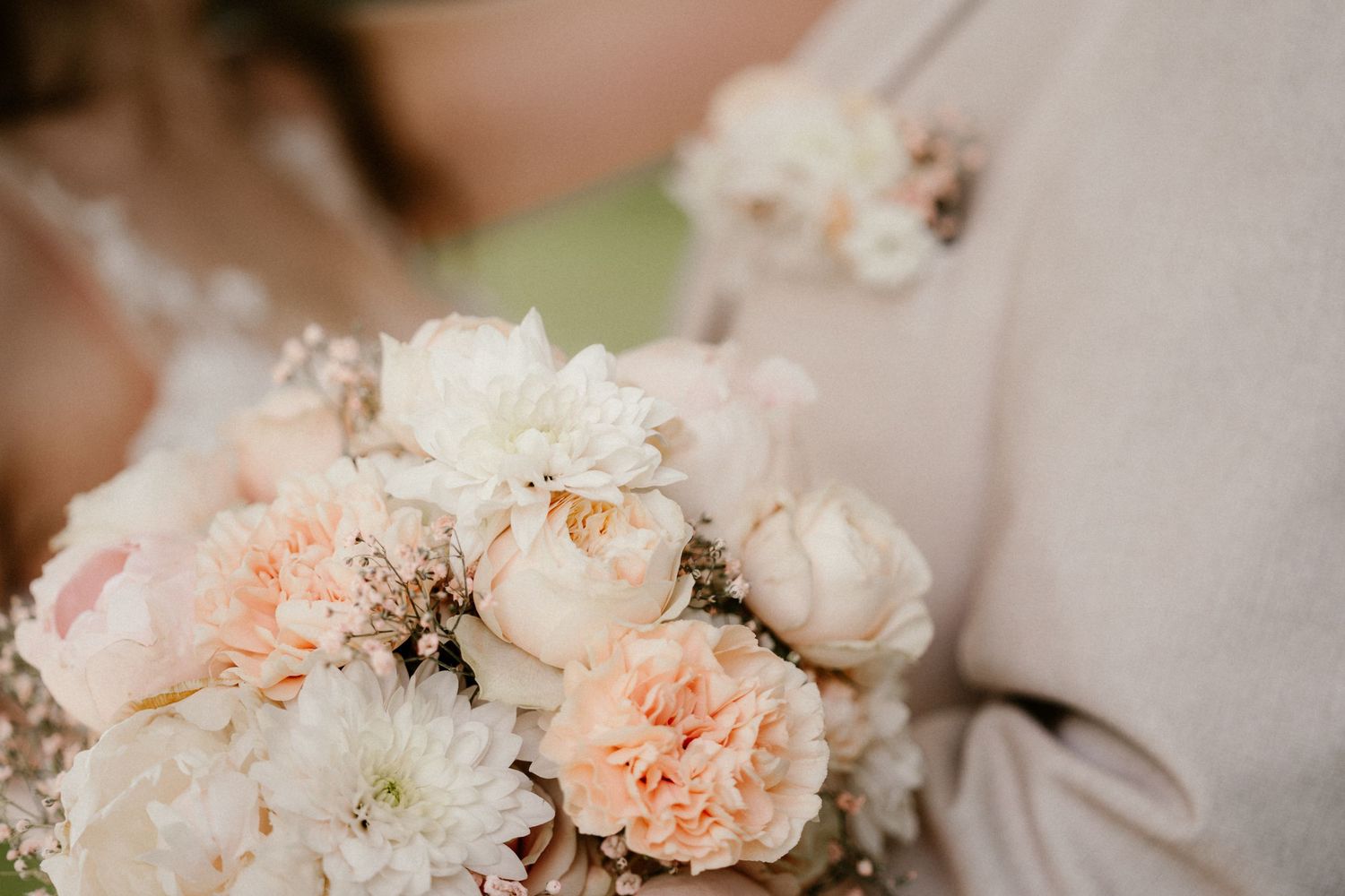 A delicate wedding bouquet featuring soft peach carnations and white roses in a romantic pastel arrangement.
