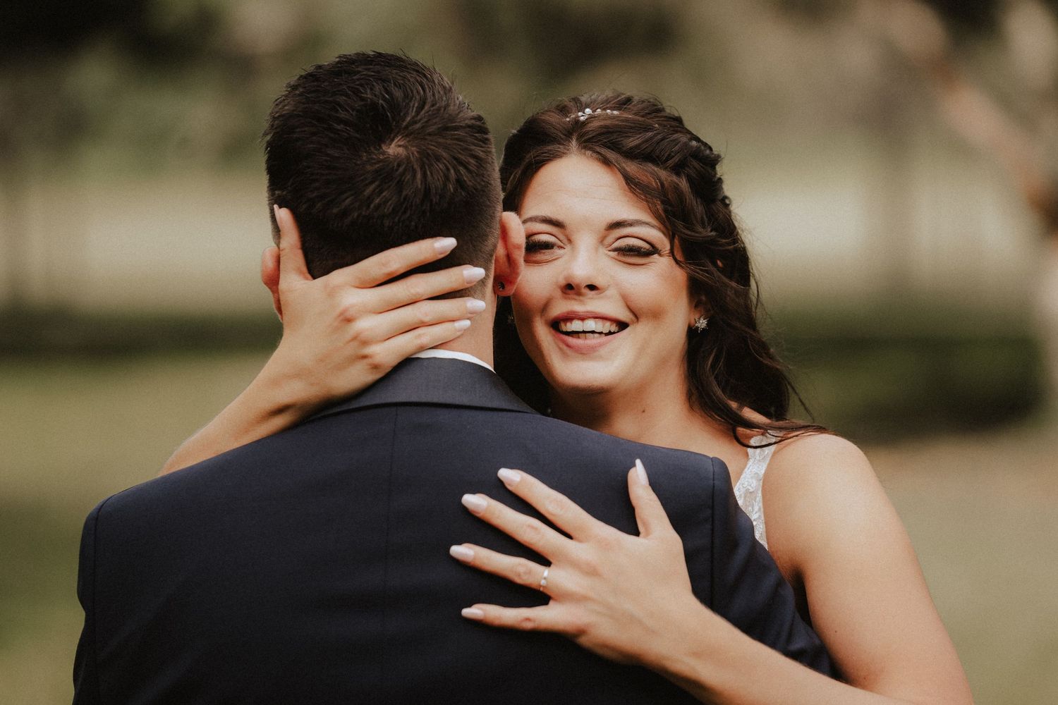A radiant bride embraces her groom in a navy suit during an outdoor wedding photoshoot.