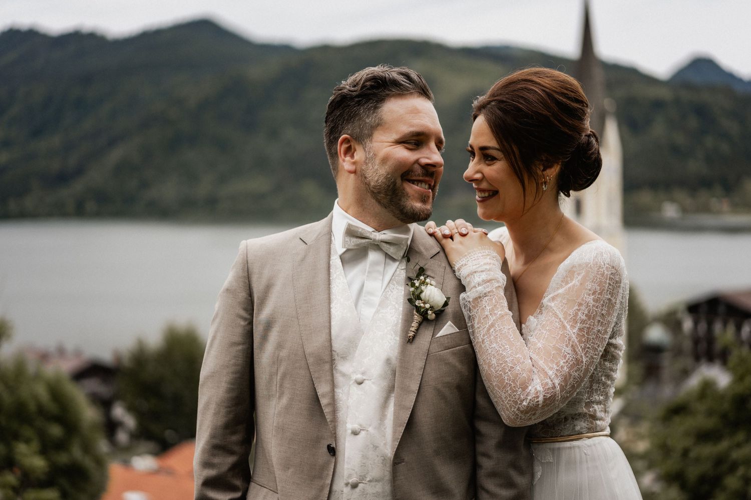 A couple shares a joyful moment on their wedding day with mountains and a lake in the background.