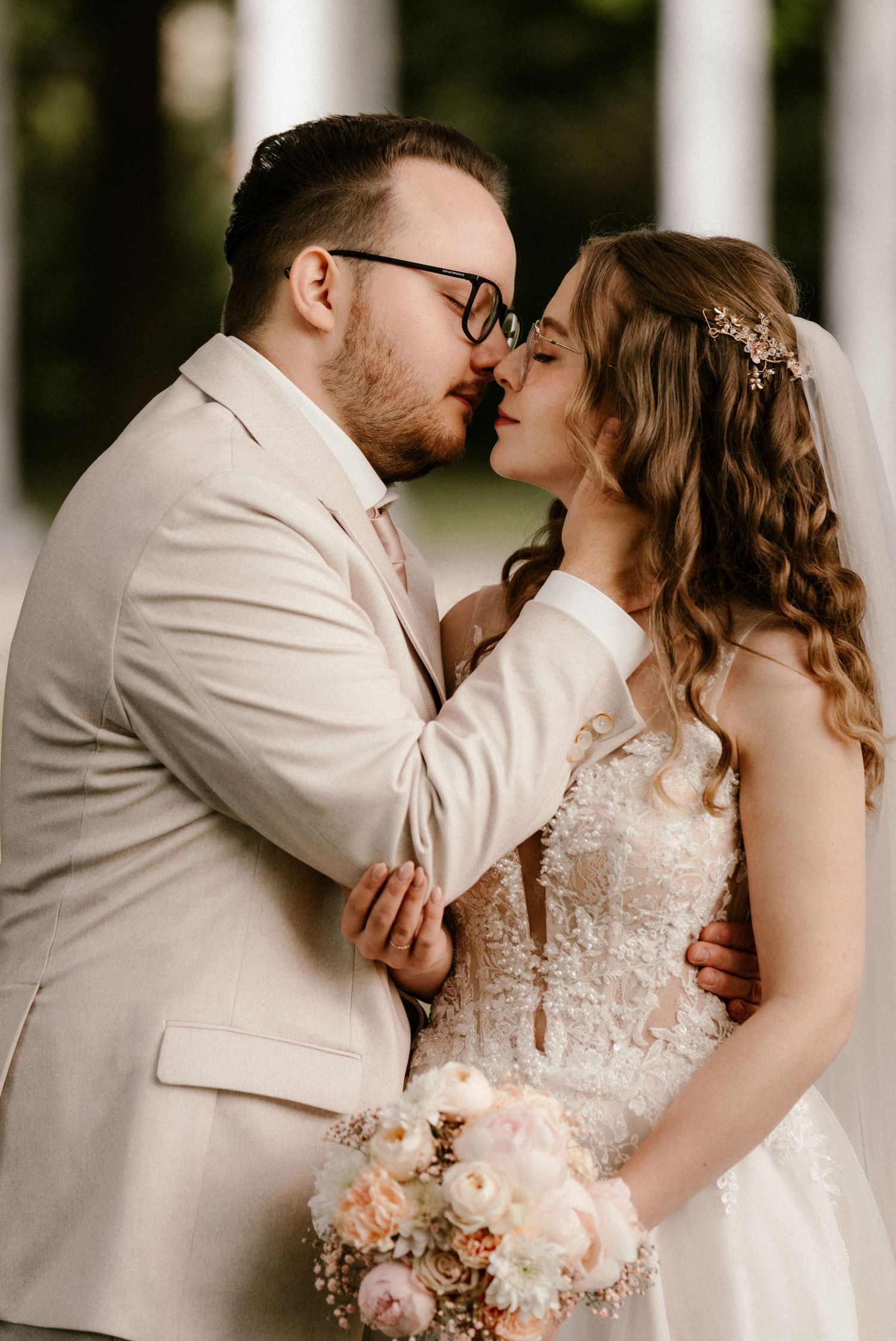 Romantic newlywed couple shares a tender kiss at their wedding, bride holding blush pink bouquet.
