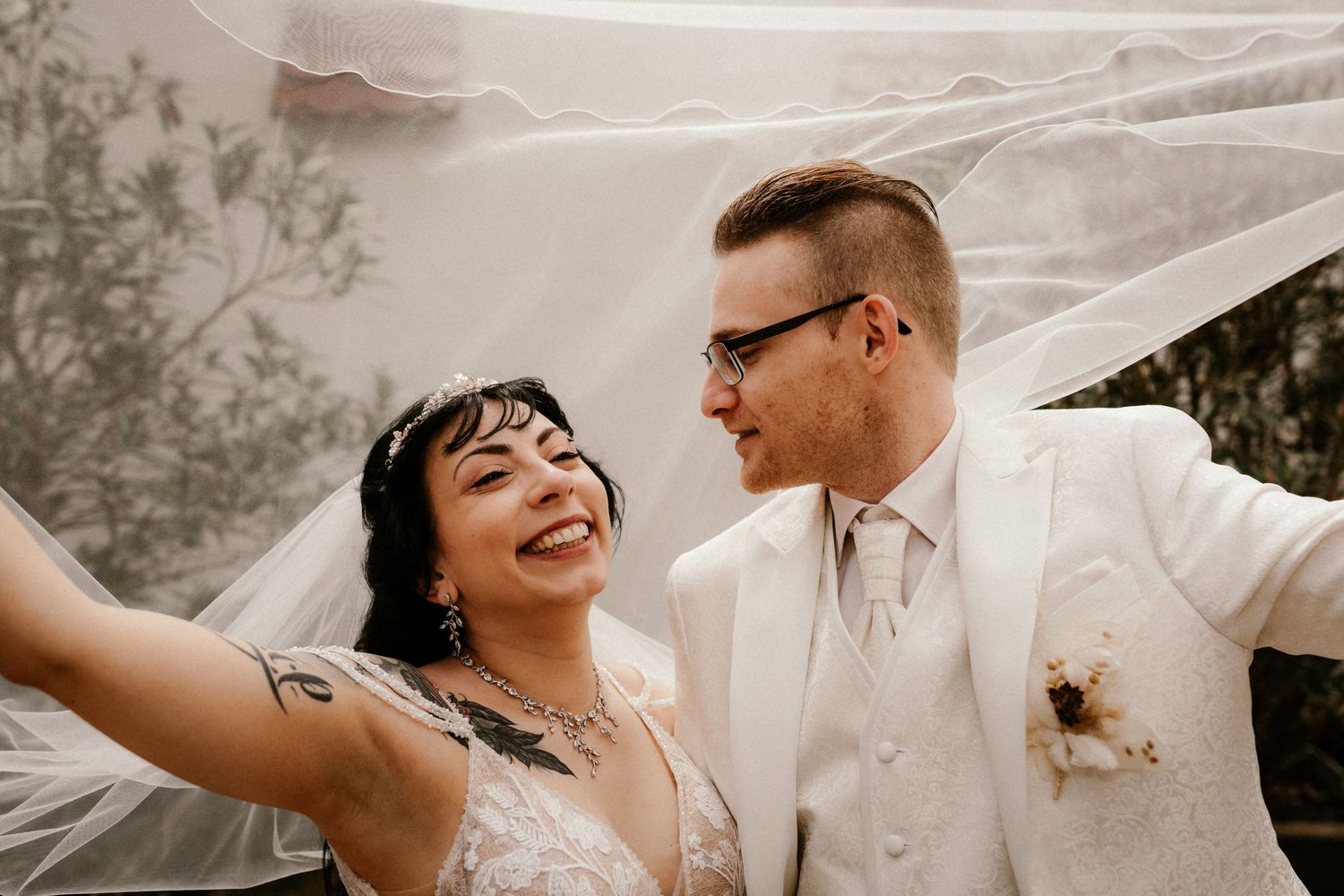 A joyful couple celebrates their wedding day outdoors with a flowing veil and vintage-inspired aesthetic.