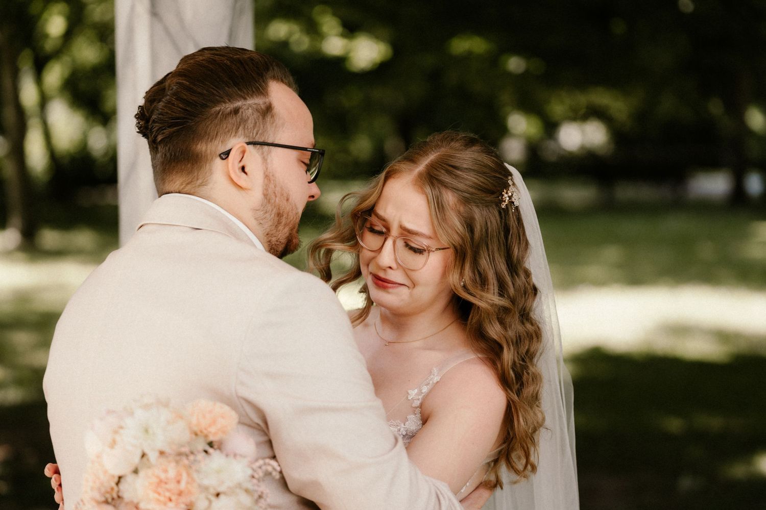 A couple shares a joyful embrace during their outdoor wedding ceremony, surrounded by dappled sunlight and greenery.